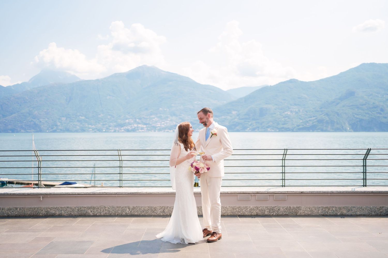 Bride and groom share a romantic moment on a lakeside terrace with stunning mountain views in the background.