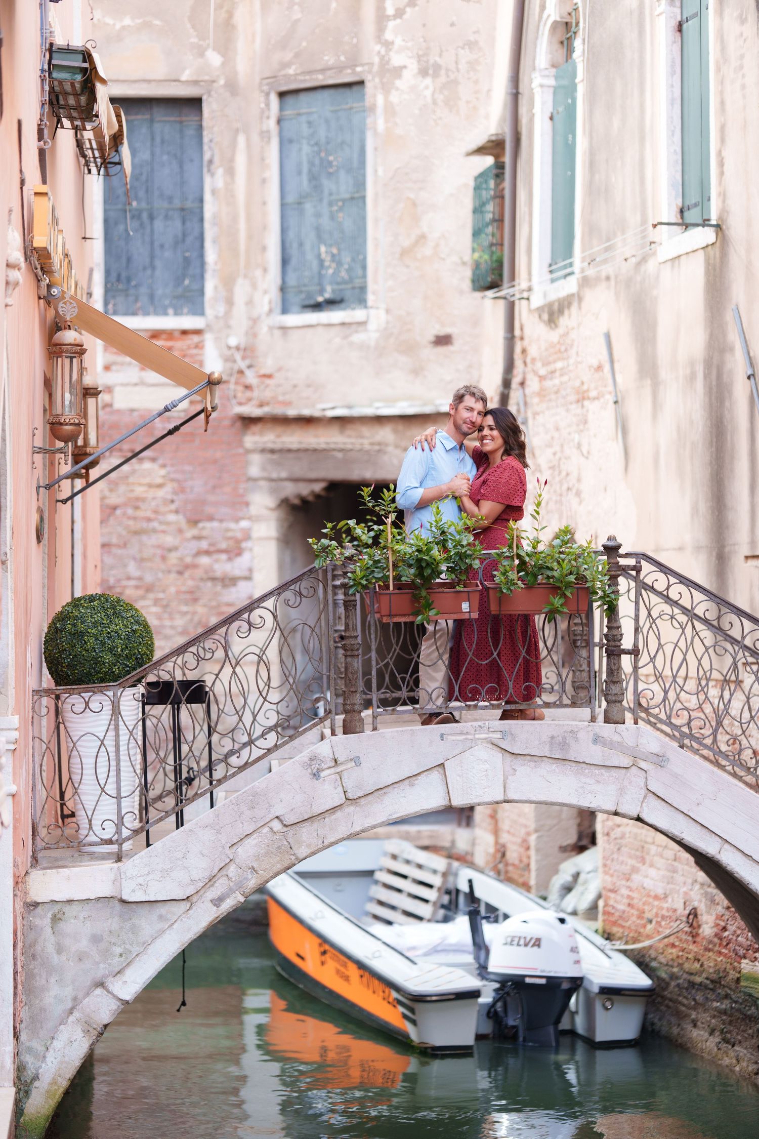 Romantic couple embracing on a charming stone bridge over a Venice canal with boats below.