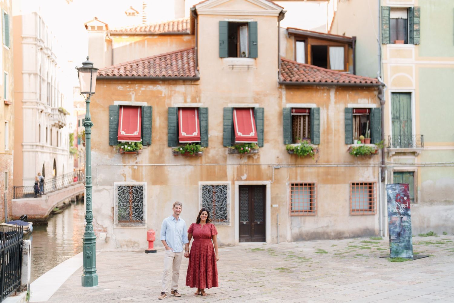 Couple posing hand-in-hand in front of a charming Venetian building with green shutters and flower boxes in Venice, Italy.