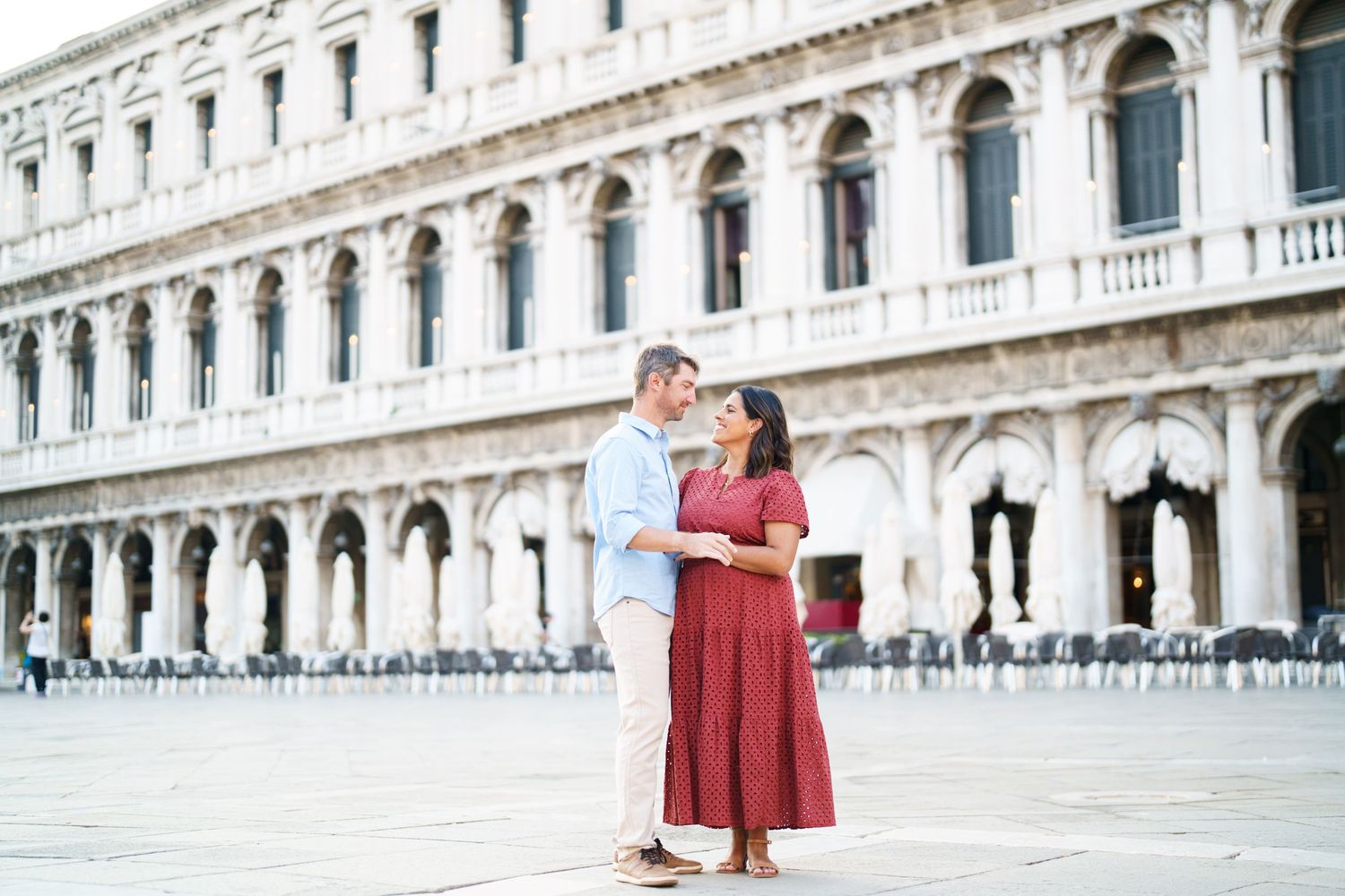 A couple shares a romantic moment in St. Mark's Square, Venice, with historic arcaded buildings in the background.