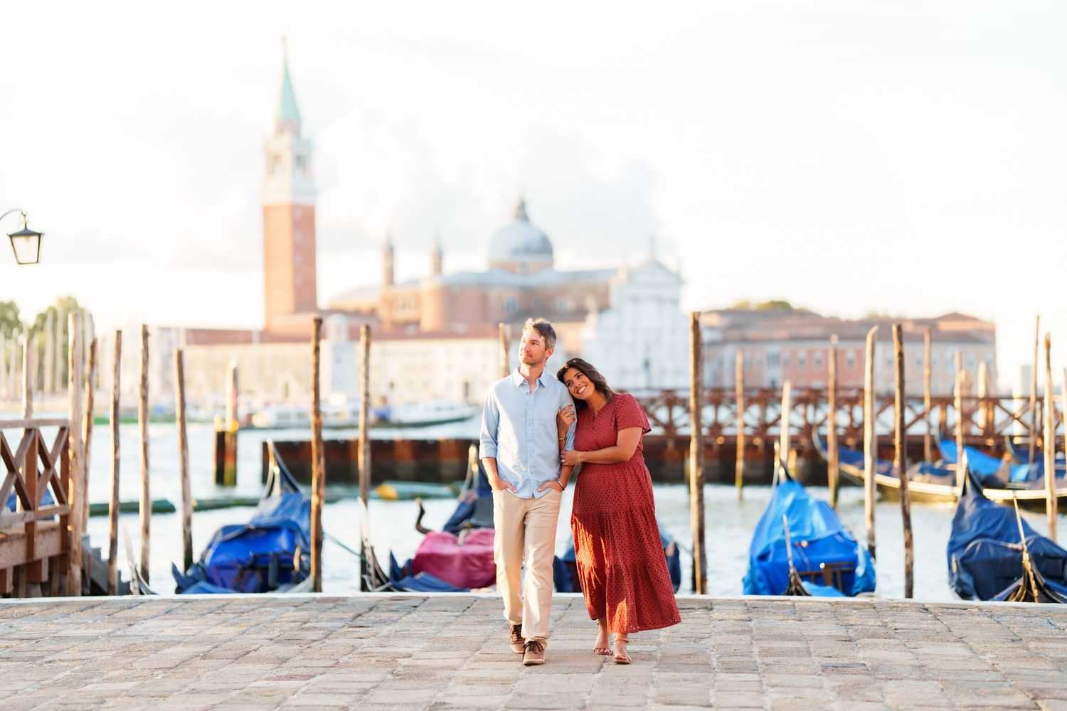 Couple strolling along Venice waterfront with gondolas and San Giorgio Maggiore church in background.