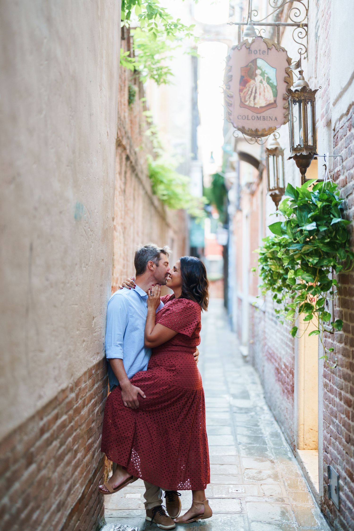 Couple sharing a romantic kiss in a narrow European alley beside Hotel Colombina sign and vintage lantern.