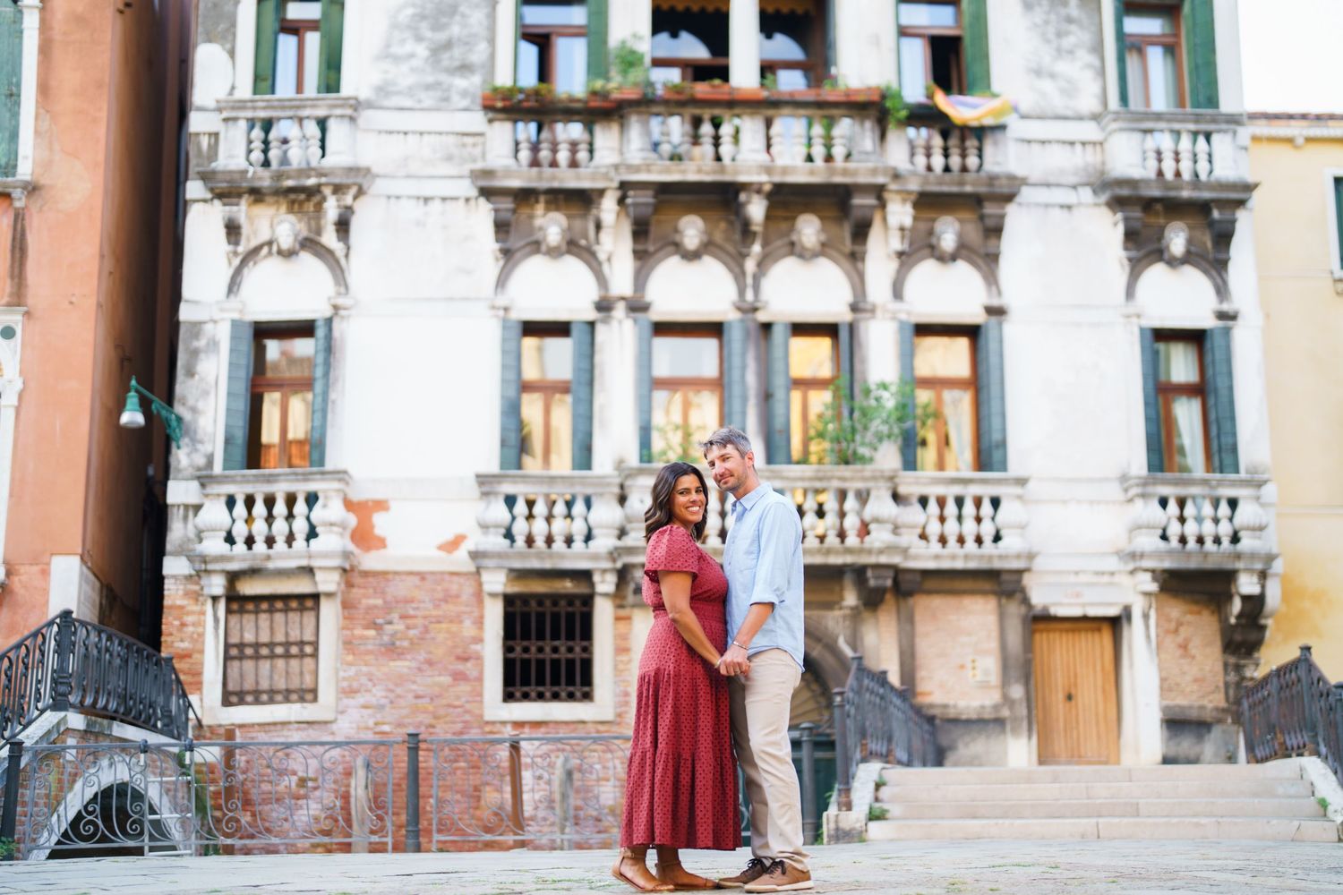 Couple embracing in front of ornate Venetian building with white balustrade in Venice, Italy.