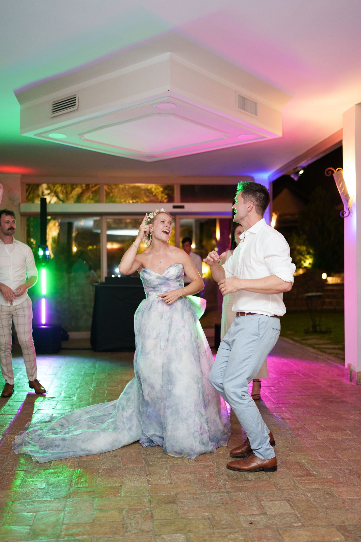Bride and groom dancing joyfully at their wedding reception under colorful lights on an outdoor dance floor.