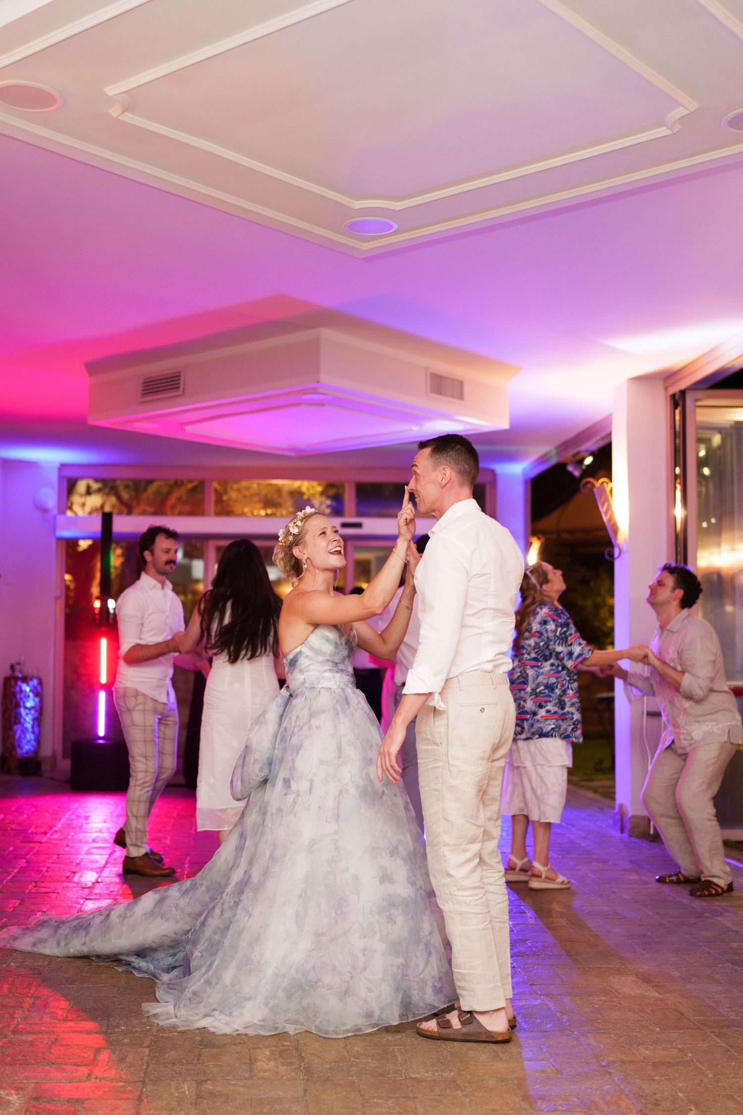 Bride and groom share first dance at wedding reception with colorful purple and pink lighting.
