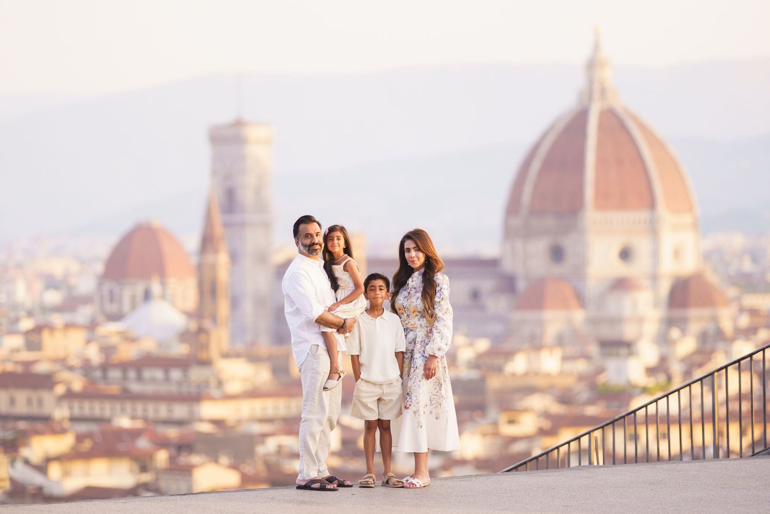 Family of four posing in front of Florence Cathedral and city skyline, wearing white outfits on a sunny day.