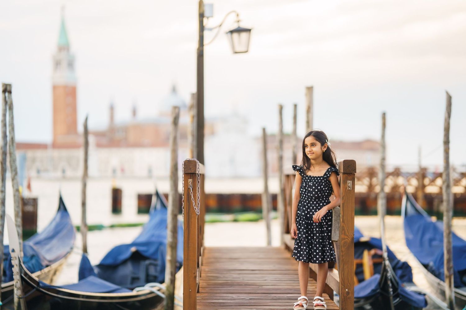 Young woman in polka dot dress standing on Venice gondola dock with St. Mark's Campanile in background.