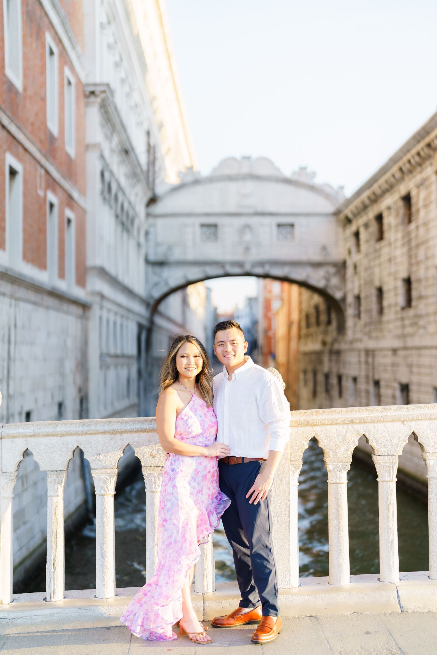 Couple posing on a bridge in Venice, Italy, with the iconic Bridge of Sighs and canal in the background.