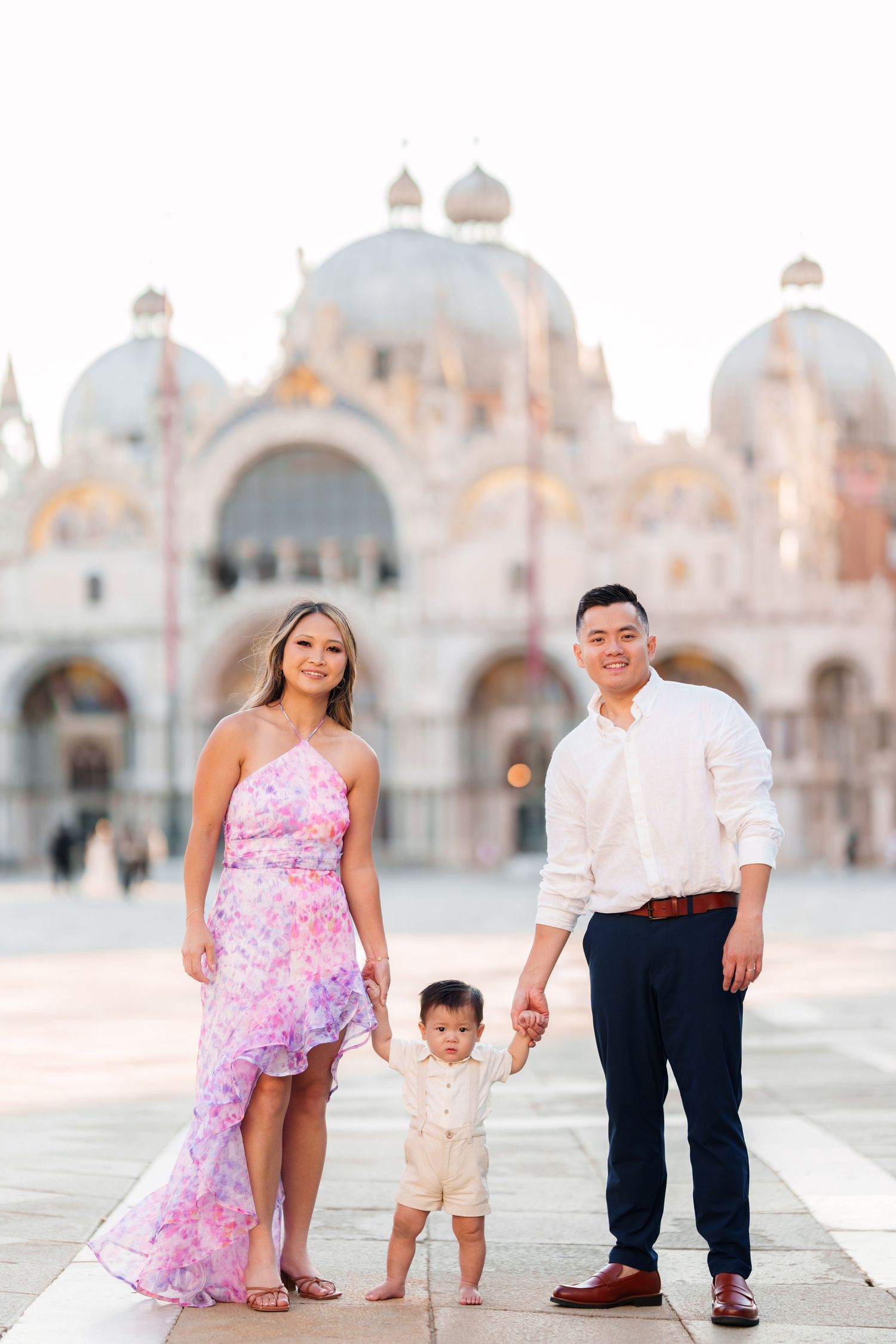 Family of three posing in St. Mark's Square, Venice, with the iconic Basilica di San Marco in the background.