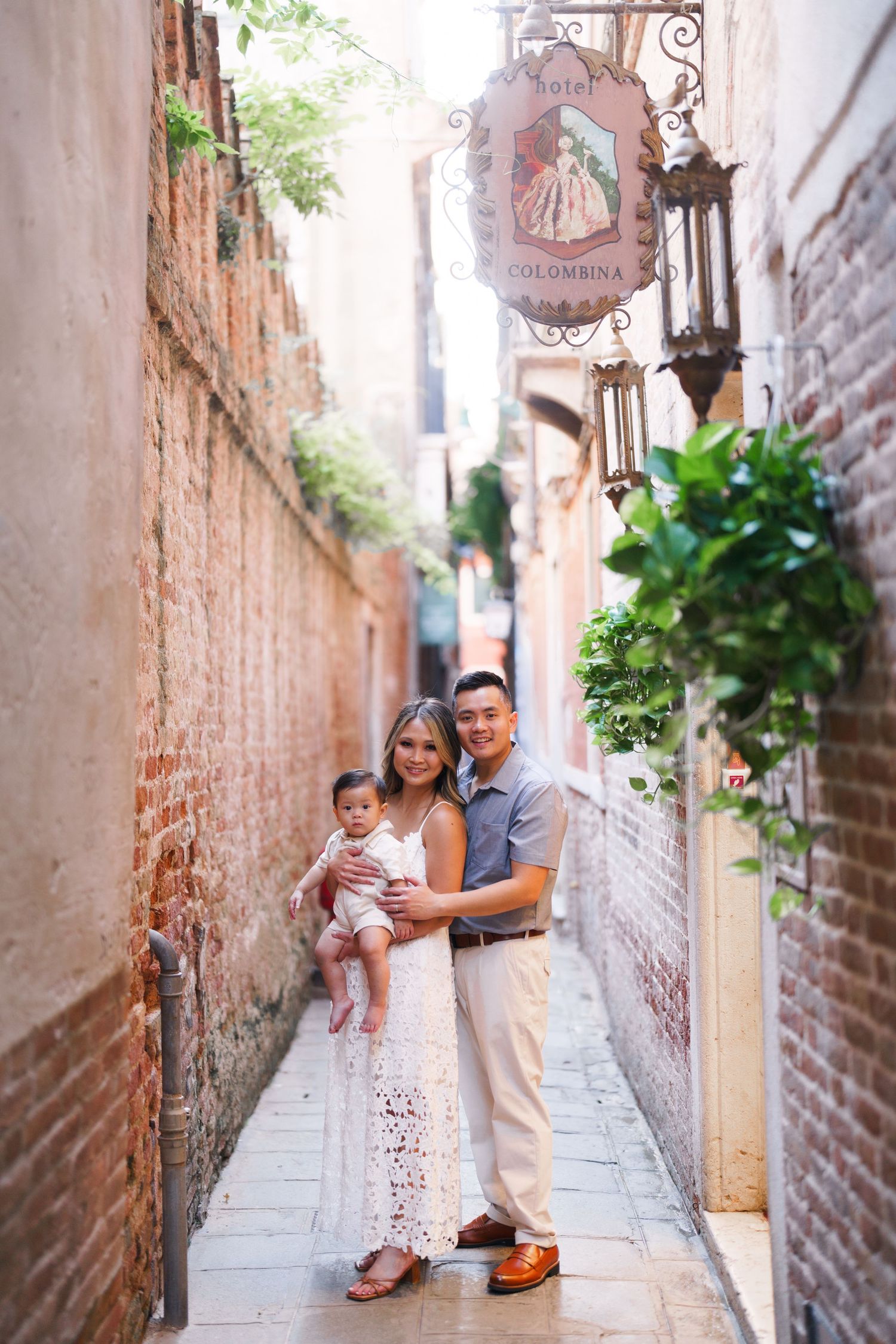 Family posing in a narrow Venice alley near Hotel Colombina, parents holding baby girl in white dress.