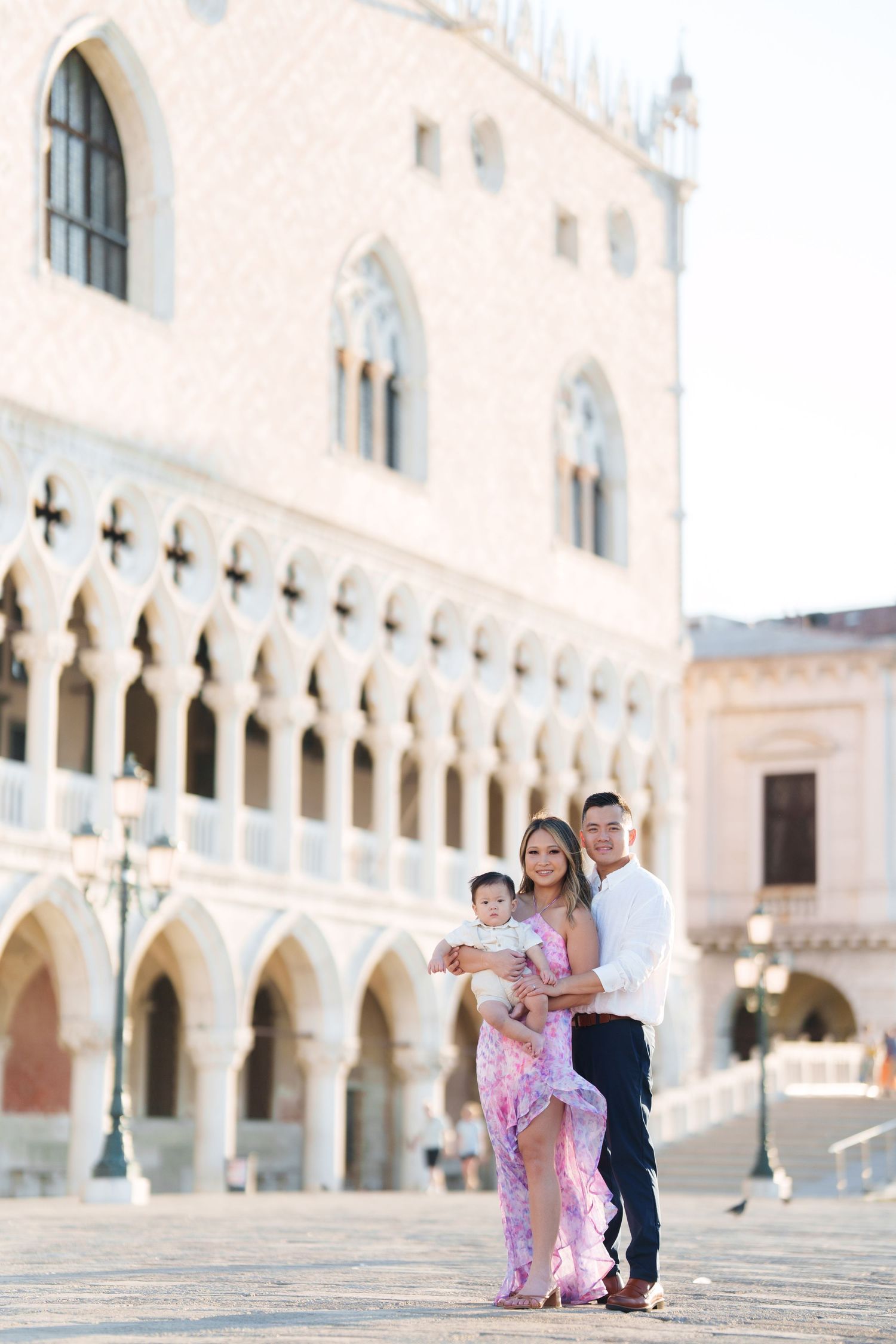 Family posing in front of the Doge's Palace in Venice, Italy, with a woman in a pink dress holding a baby.
