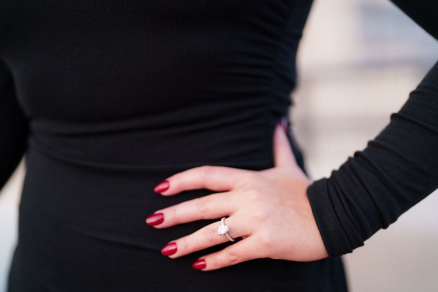 Close-up view of hands with red nail polish resting on a black fabric surface.