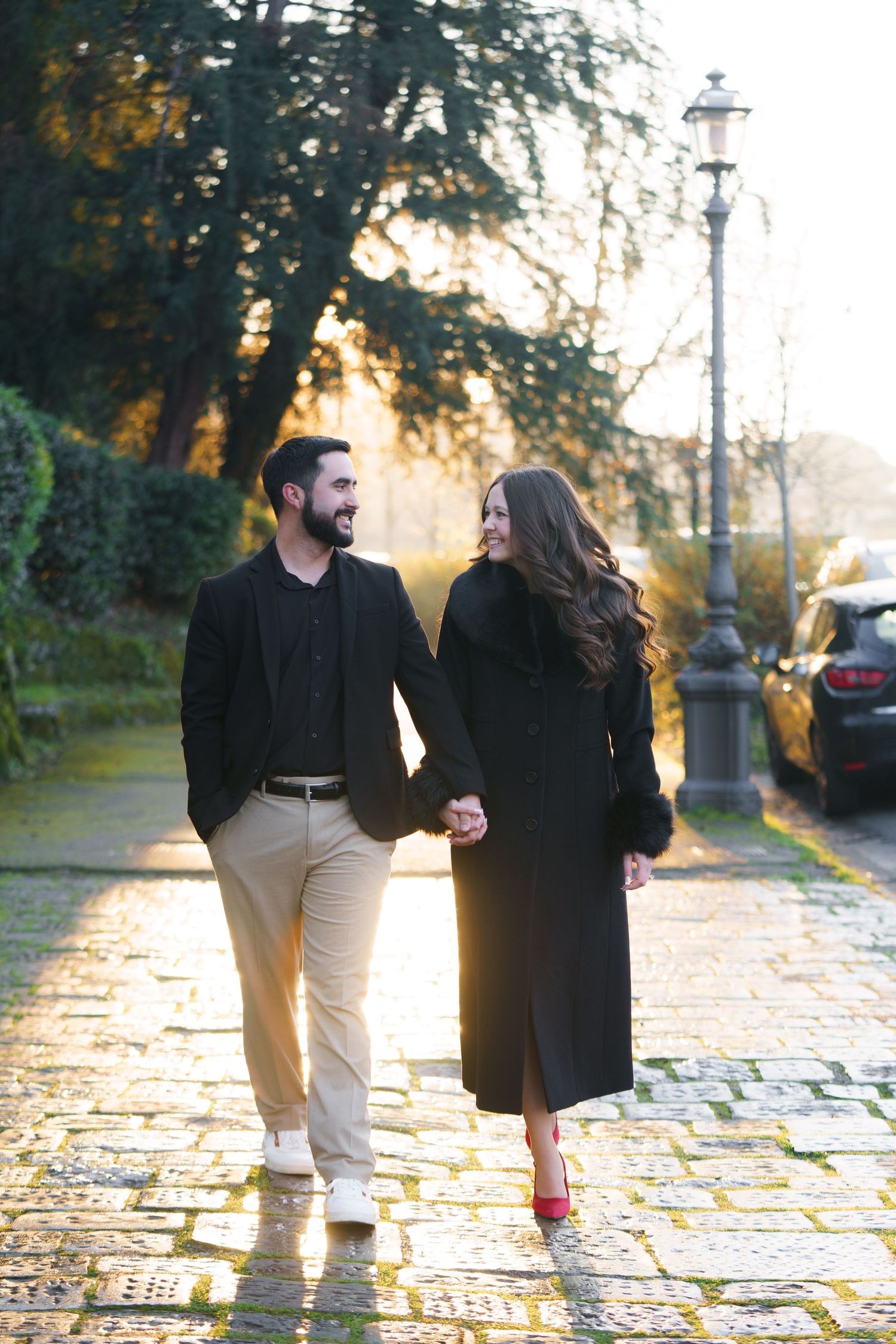 A couple walks together on a cobblestone path during golden hour, creating a romantic autumn scene.