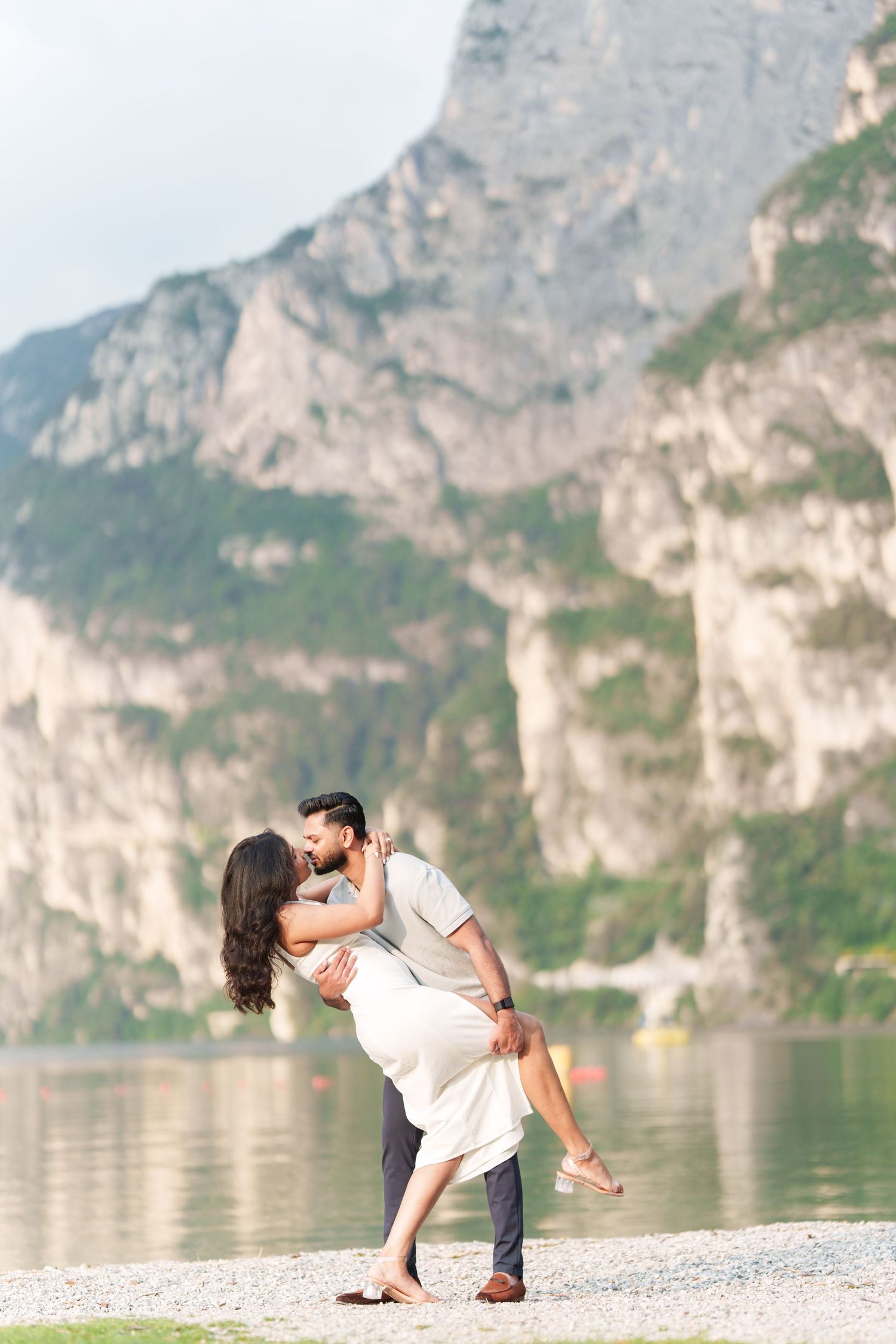 Couple shares romantic poses by a scenic mountain lake with dramatic limestone cliffs in the background.