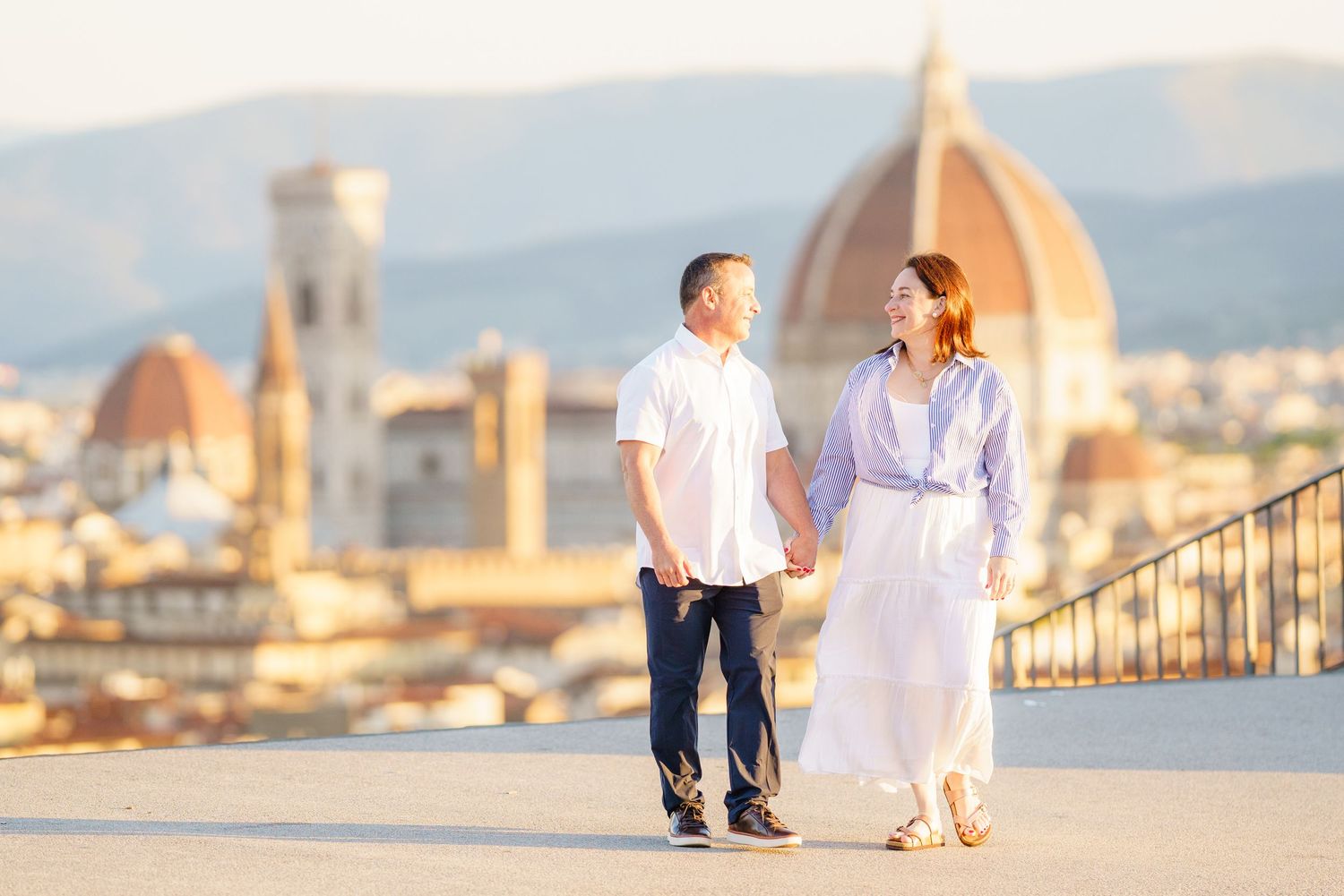 A romantic couple in white outfits poses for photos with Florence's iconic Duomo cathedral in the background at sunset.