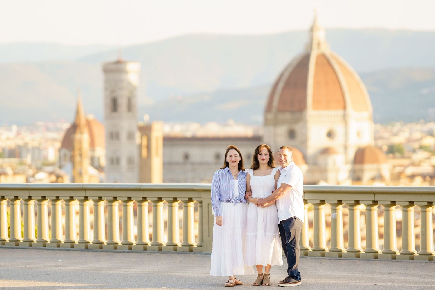 A couple in white wedding attire embraces on a scenic balcony overlooking Florence's iconic Duomo cathedral in Italy.