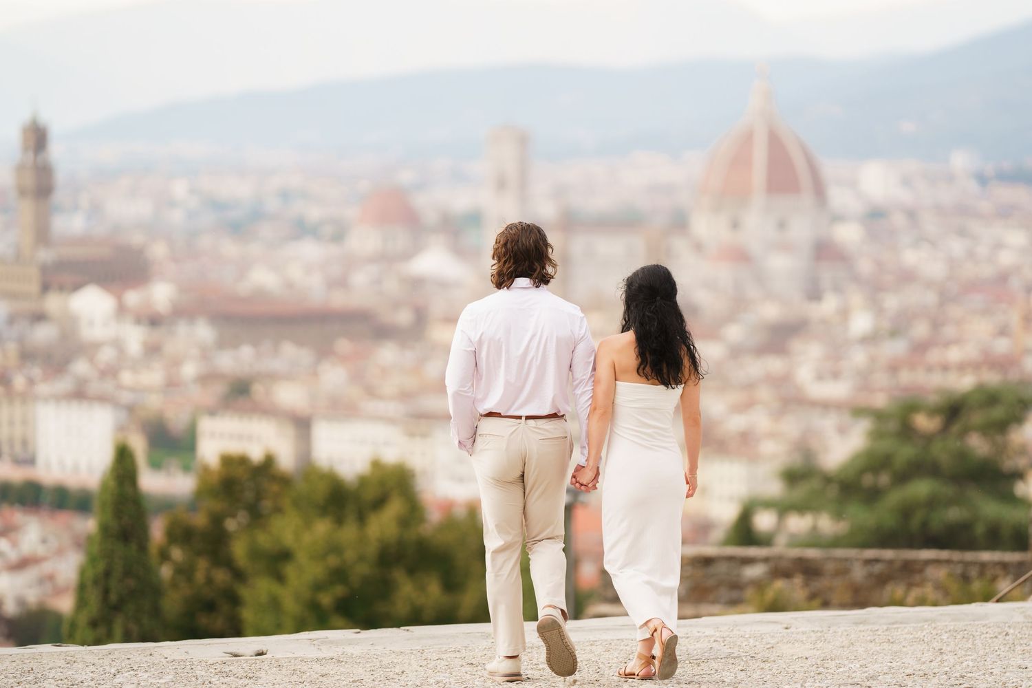 A couple stands on a scenic overlook admiring the panoramic view of Florence, Italy with its historic architecture.