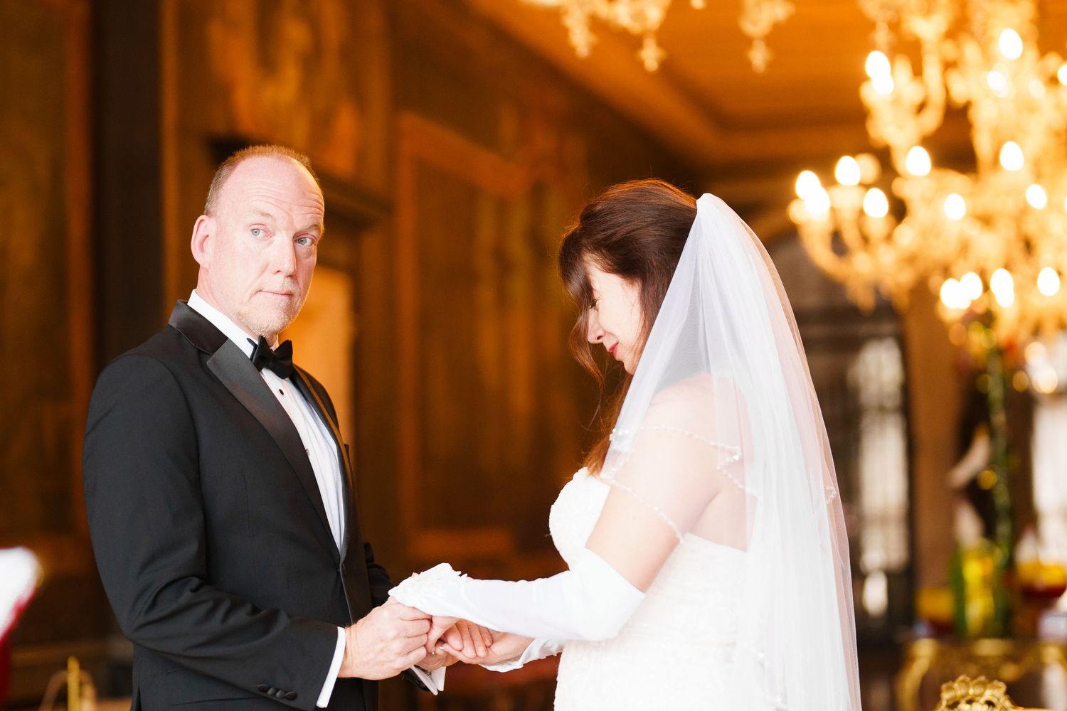 Elegant wedding ceremony takes place in a grand ballroom with ornate chandeliers and romantic lighting.