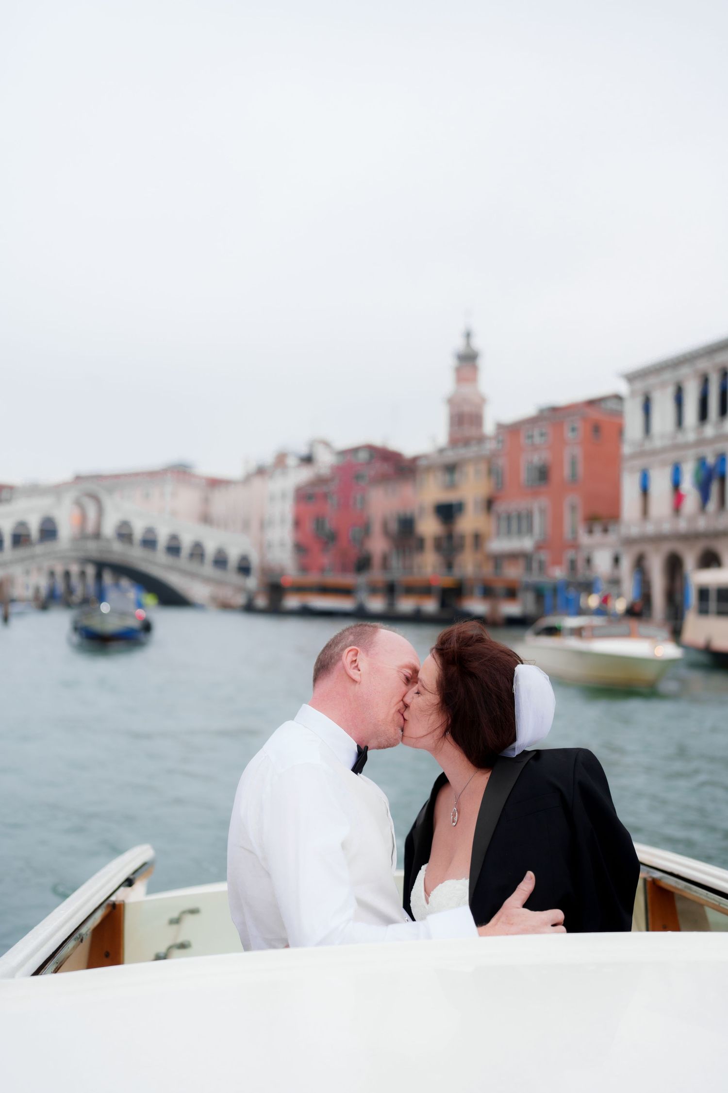A romantic moment captured on a boat in Venice's Grand Canal with historic buildings in the background.