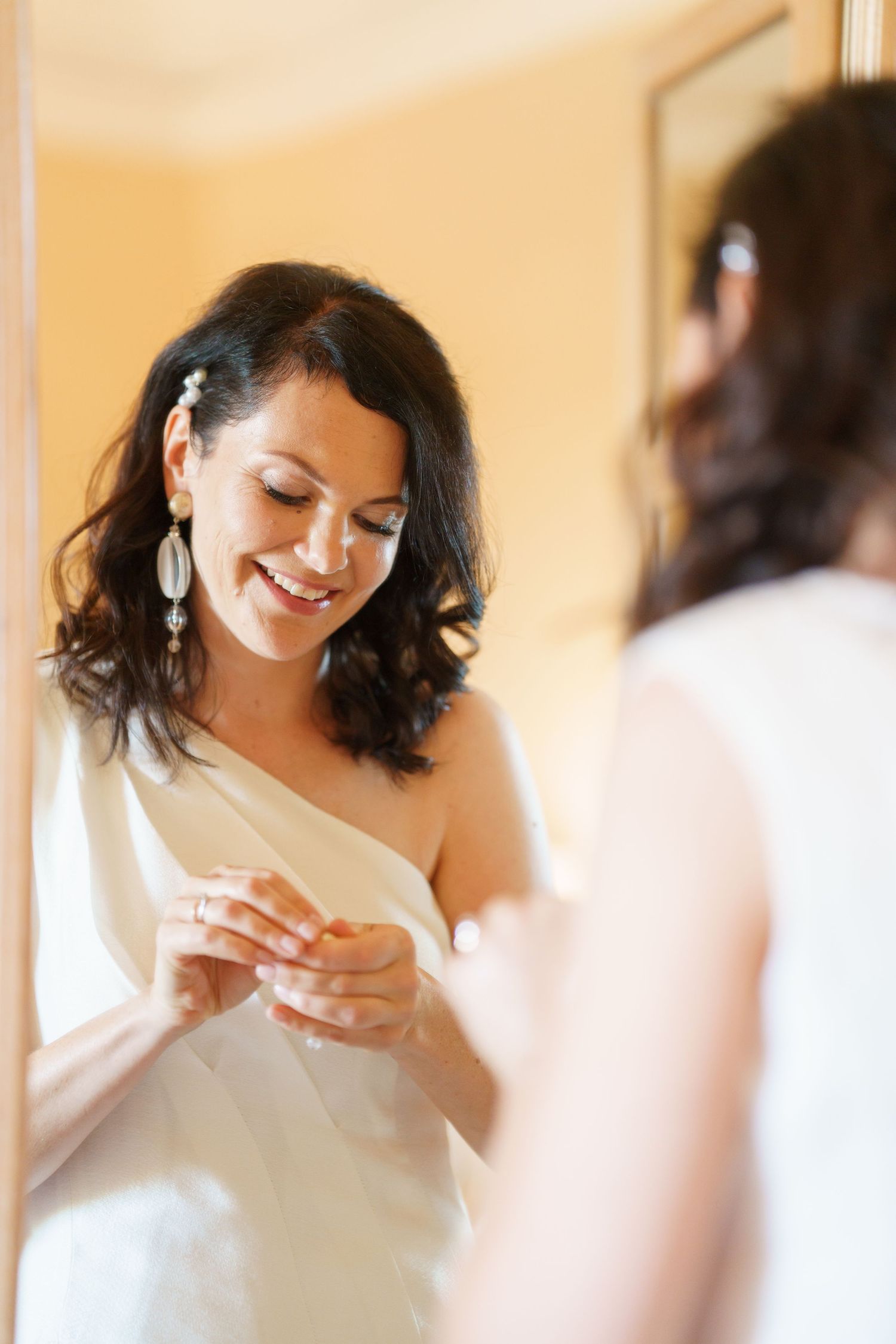 Person in white dress looking down while getting ready in a warmly lit room.