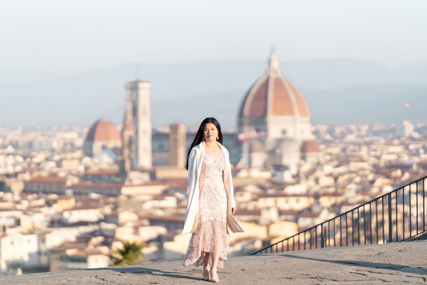 Woman in pink dress poses at scenic Piazzale Michelangelo viewpoint overlooking Florence's iconic Duomo cathedral.