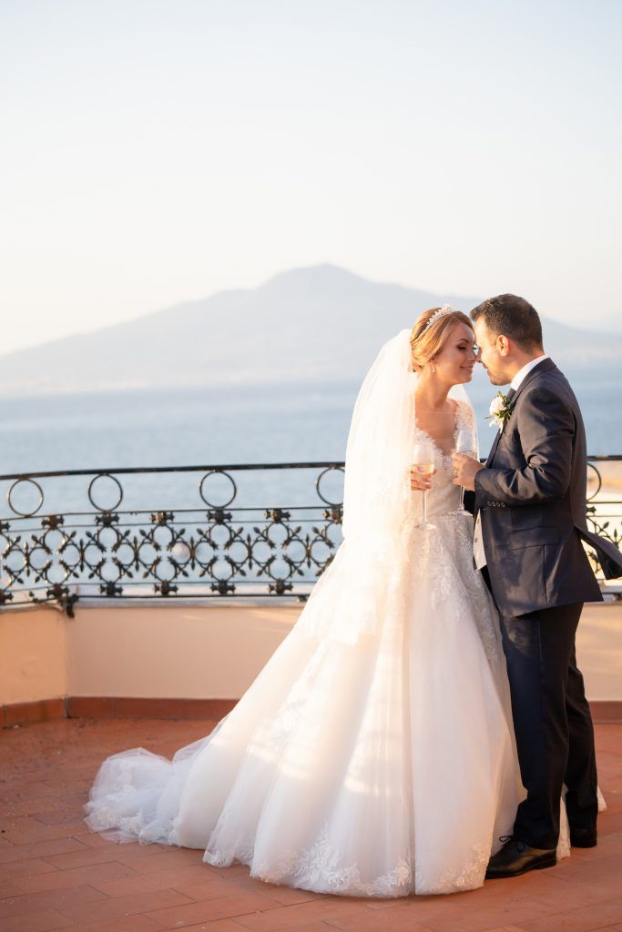 Romantic wedding moment on a seaside terrace with ornate railings and mountain views.