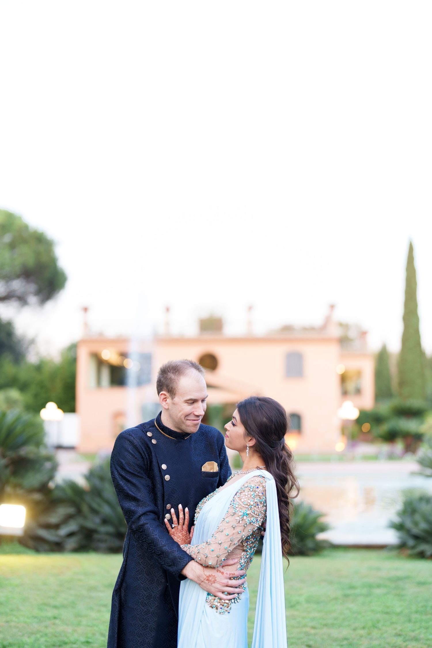 Couple sharing intimate moments on manicured lawn with Mediterranean architecture backdrop.