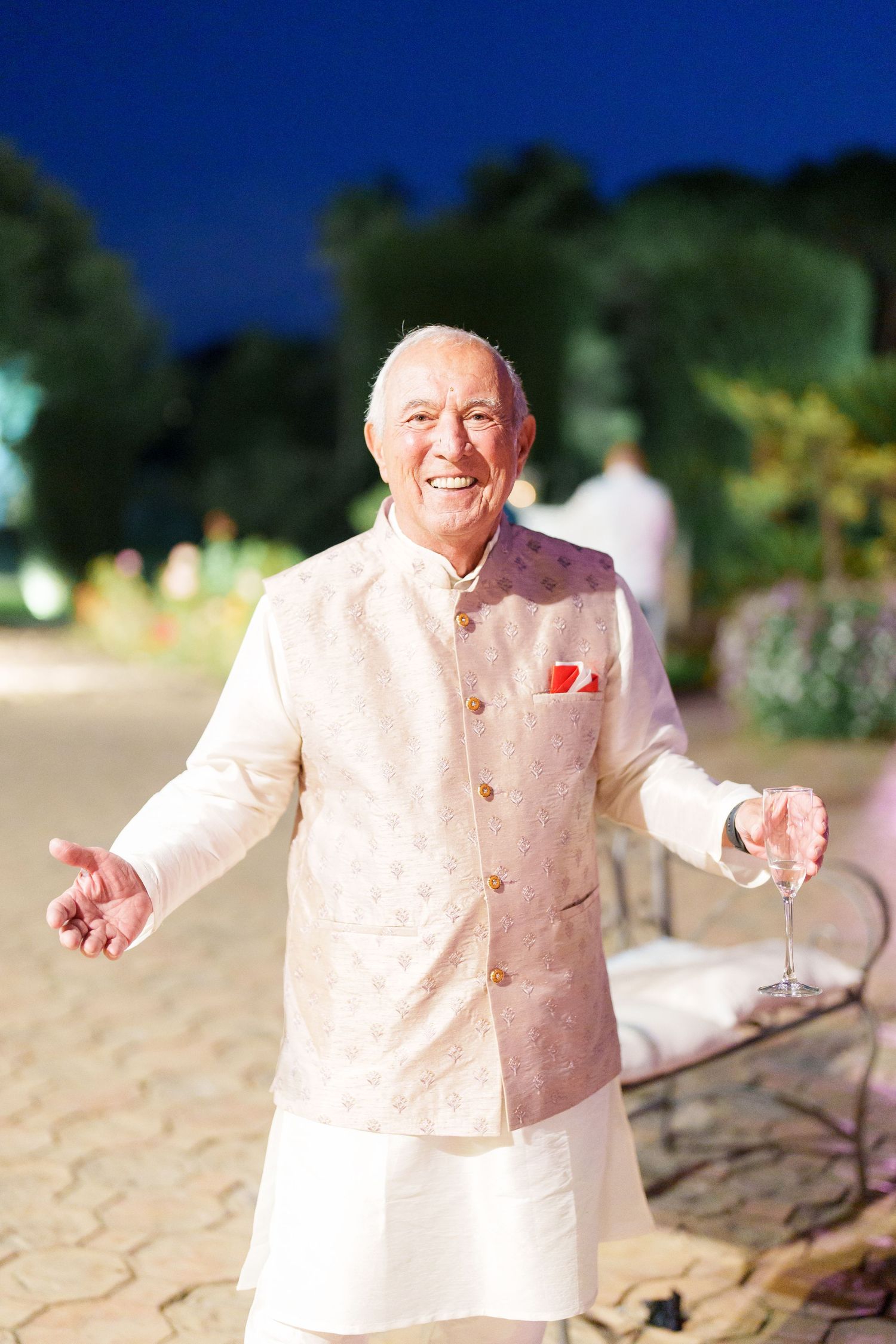 Person in light colored formal attire gesturing during an outdoor evening celebration.