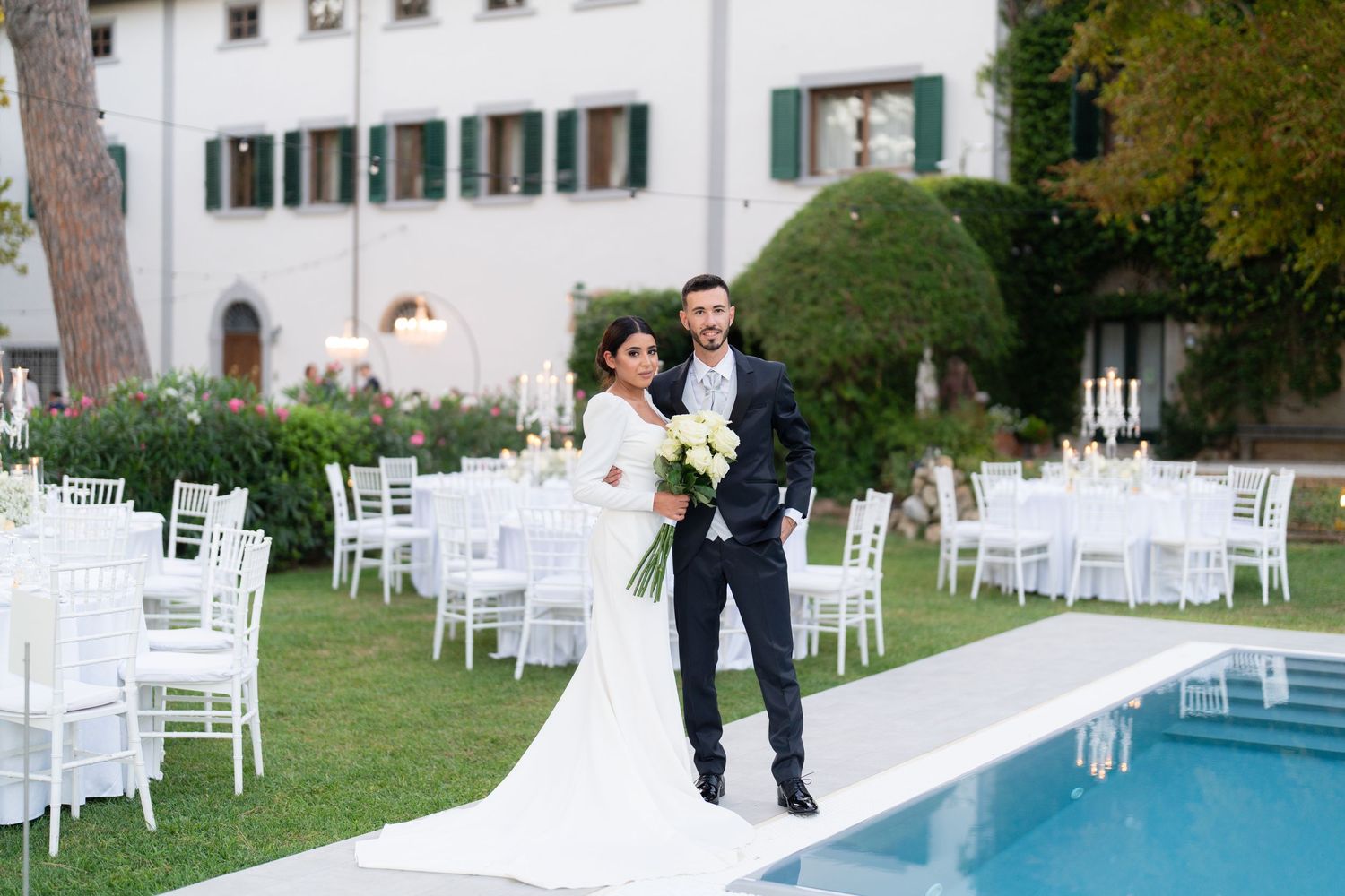 Elegant outdoor wedding reception setup with white chairs and swimming pool at a luxurious villa.