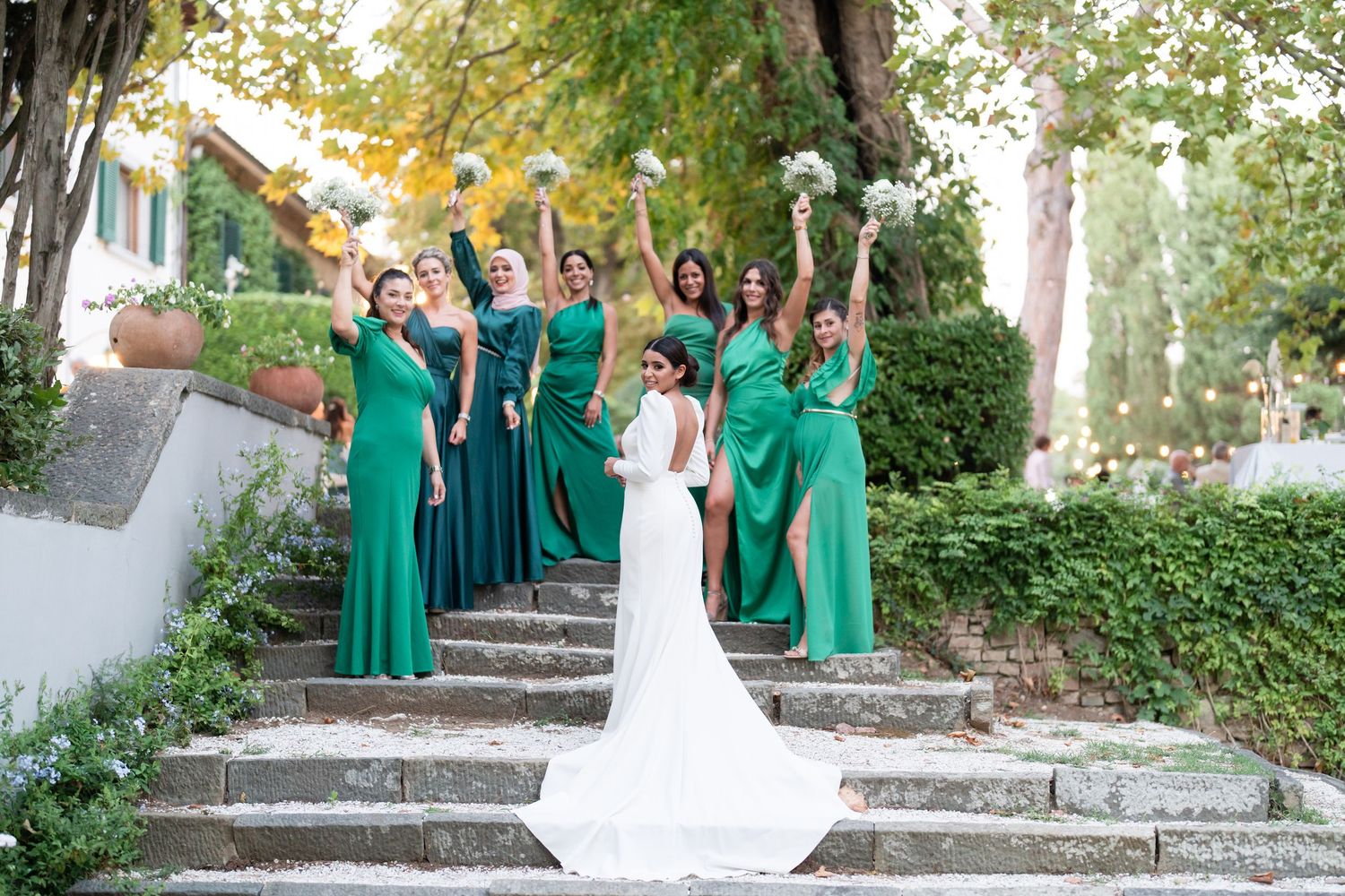 Wedding party celebrating on stone steps with bridesmaids in emerald green dresses.