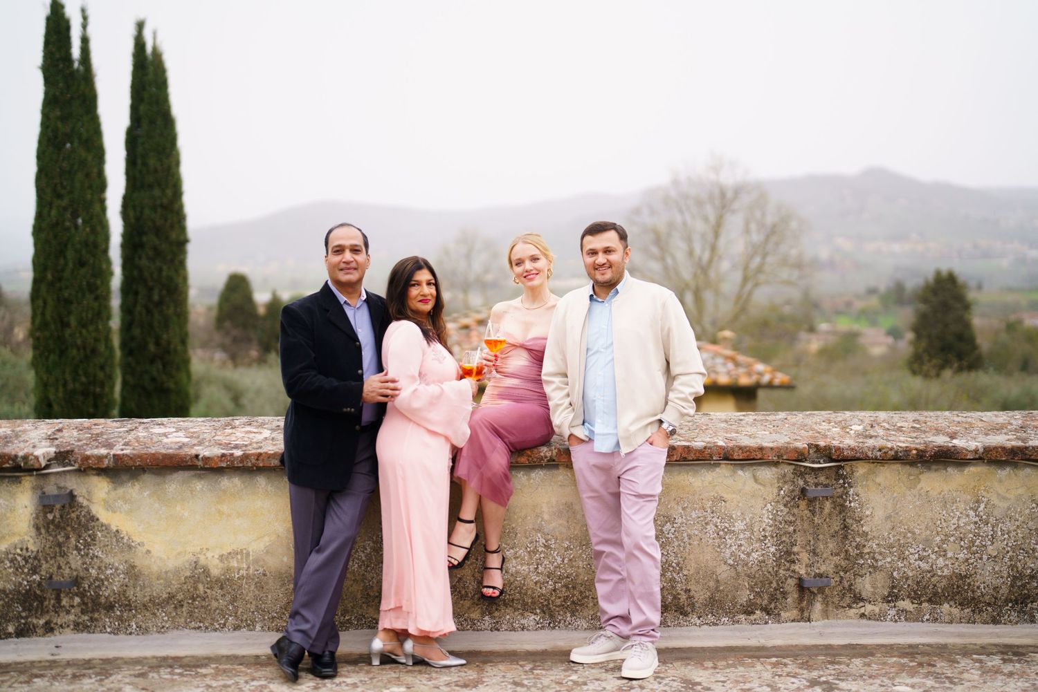 Group photo against stone wall with cypress trees and Tuscan countryside in background.