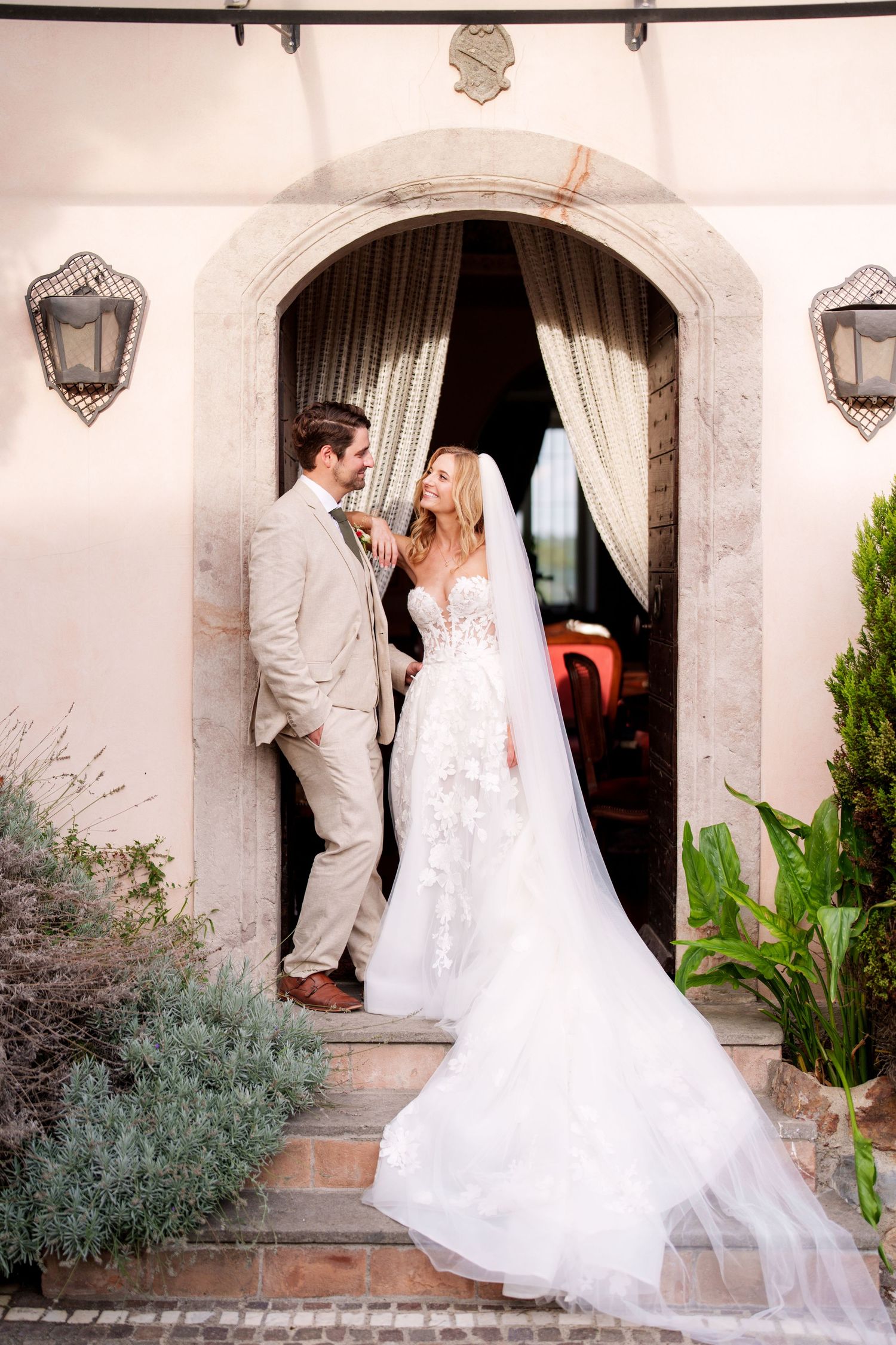 Elegant wedding couple poses in front of Mediterranean-style archway with white dress flowing.