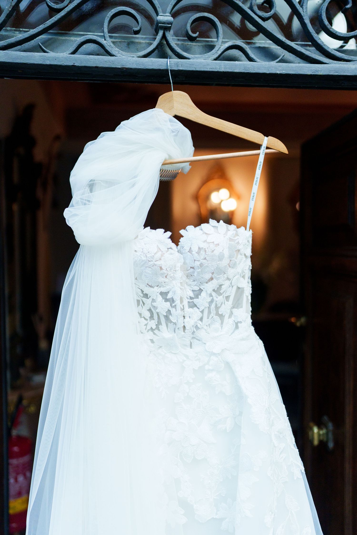 White lace wedding dresses hanging on elegant hangers against an ornate iron backdrop.