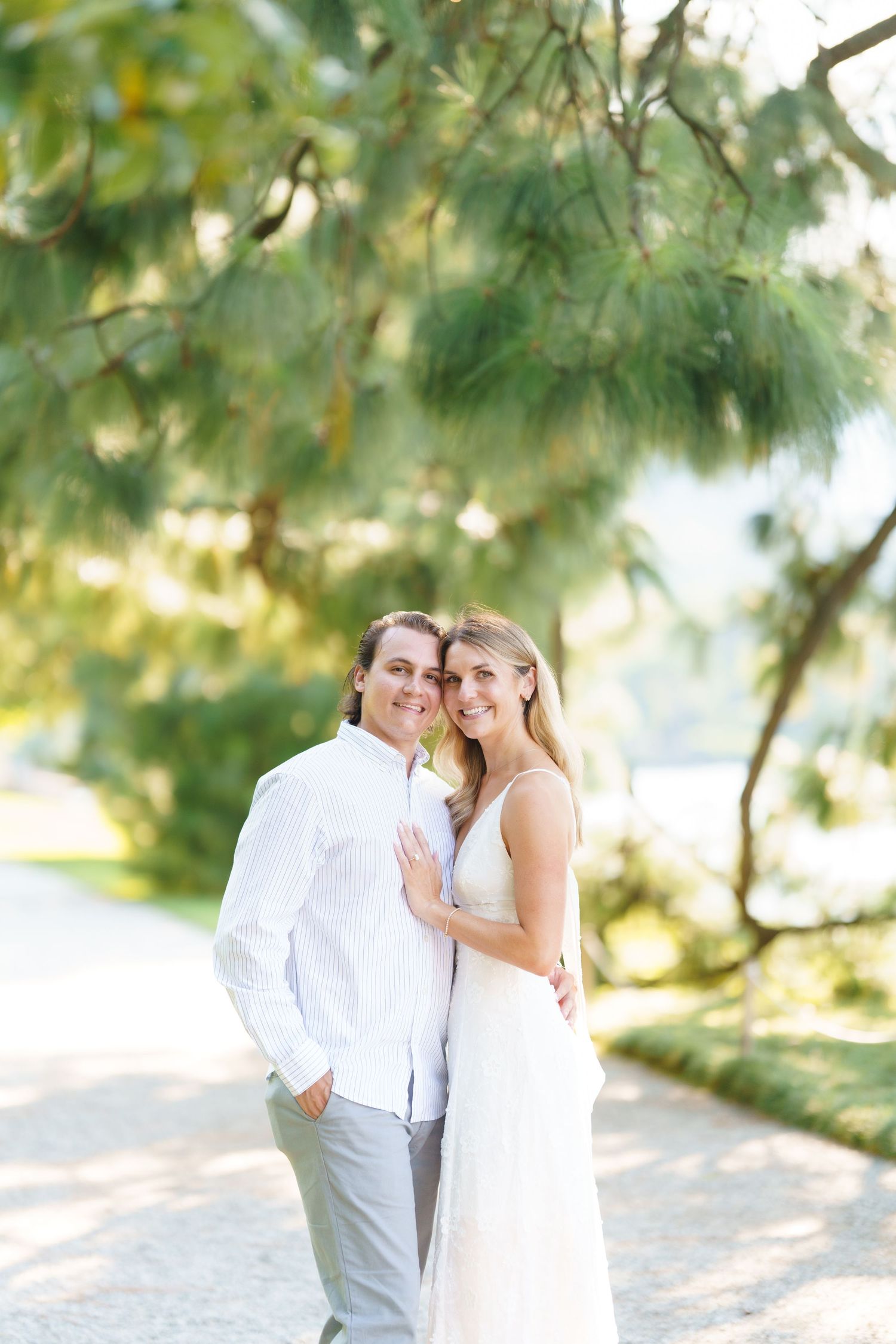 A romantic wedding couple shares an intimate moment under sunlit trees on a bright summer day.
