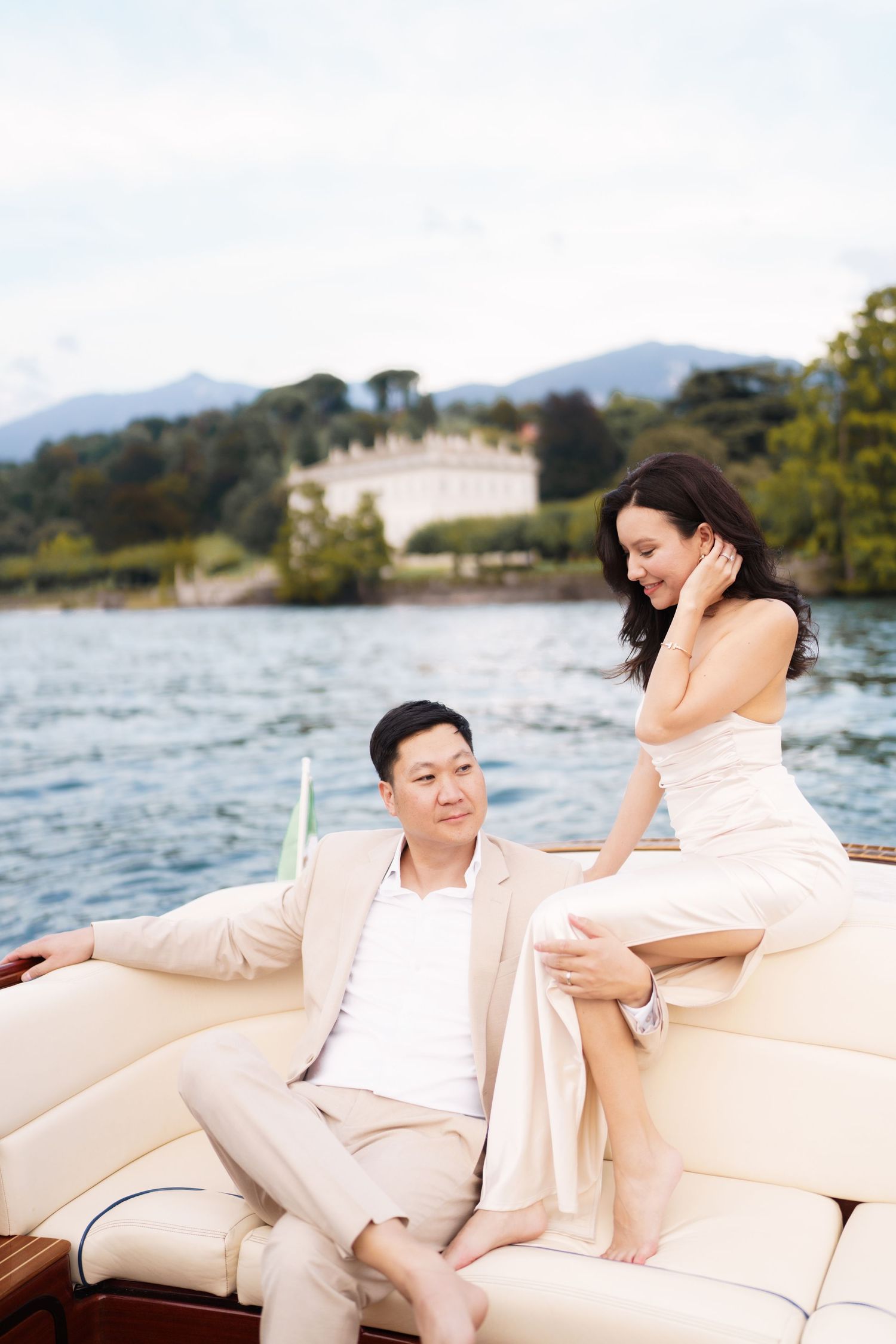 A person in white clothing lounges on a cream-colored boat cushion with a scenic lake and mountains in the background.