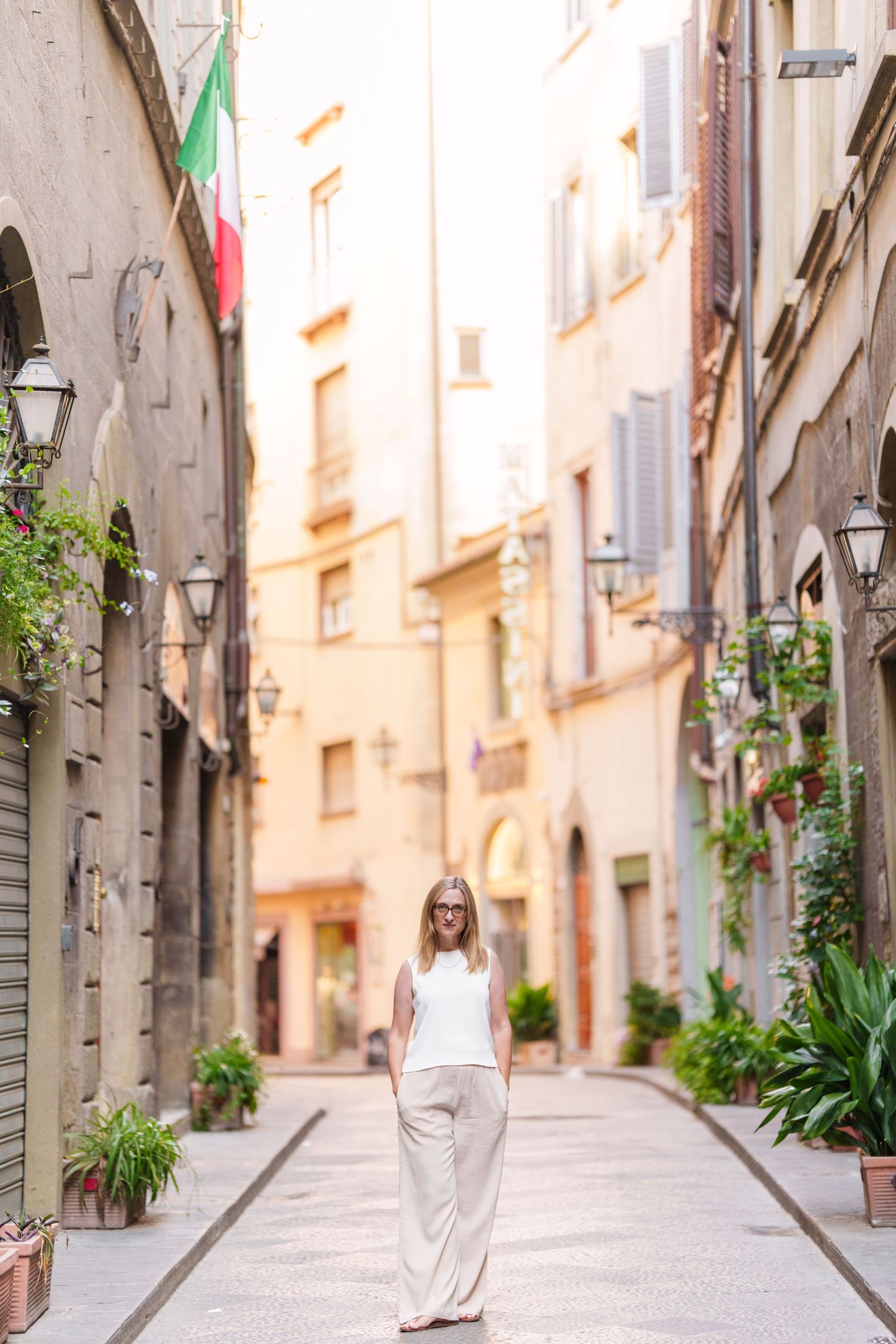 Narrow cobblestone street in an old European town with white buildings and potted plants along the walls.