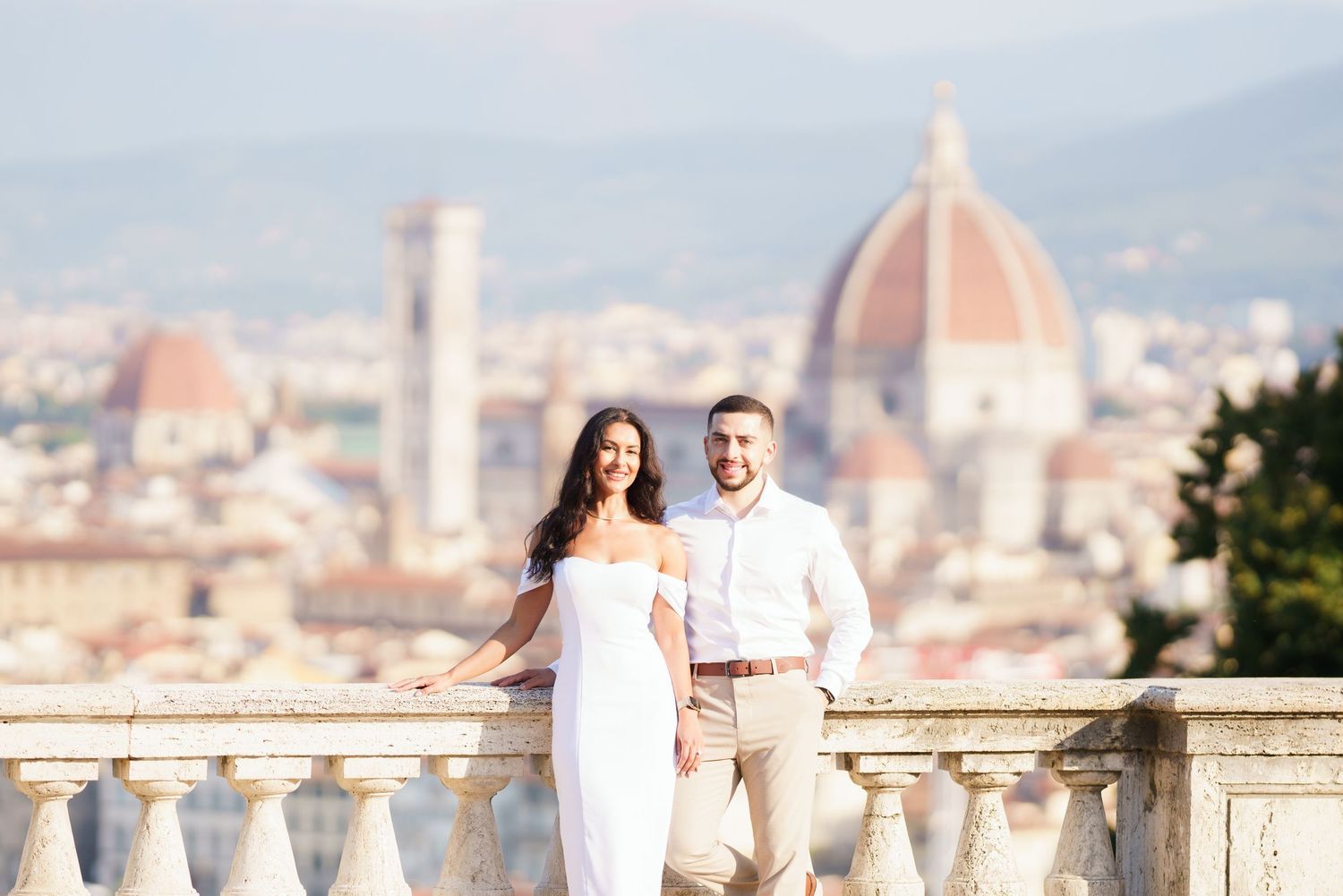 A couple poses at a scenic overlook with Florence's iconic Duomo cathedral and cityscape in the background.