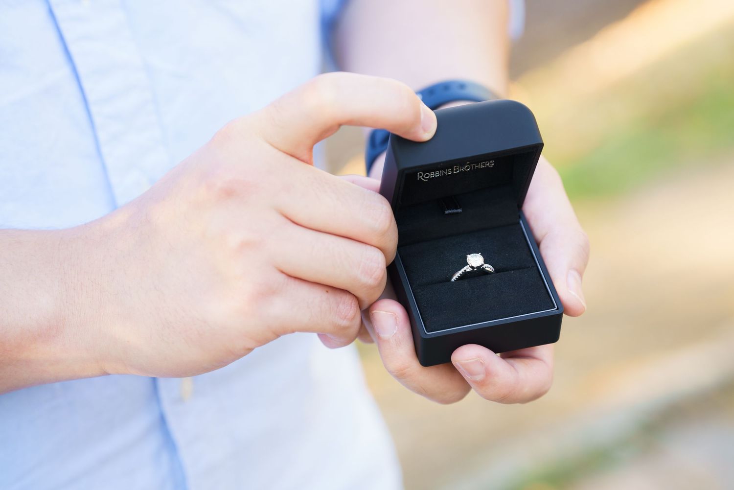 A series of hands opening a small black jewelry box showing a ring inside.