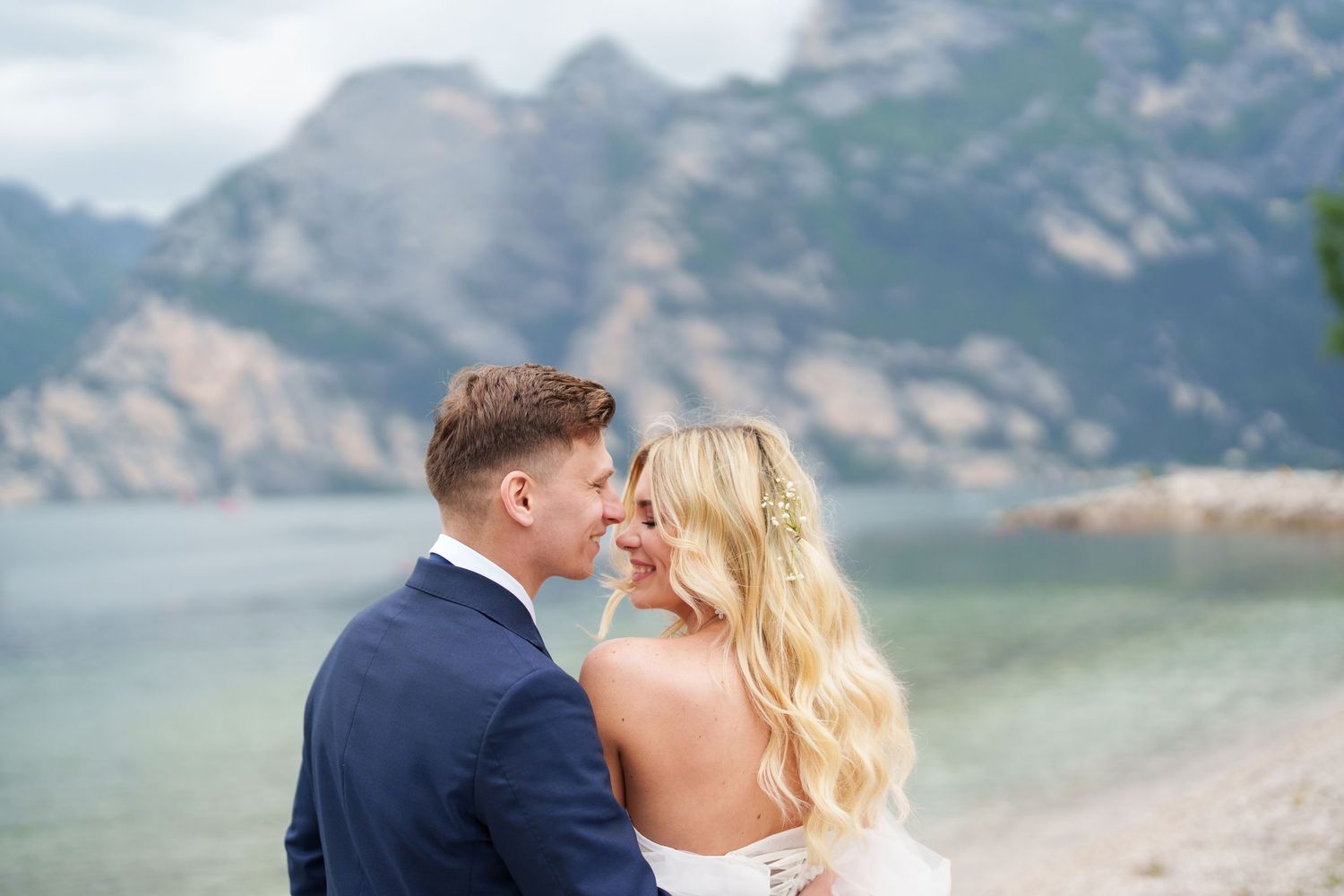 A couple shares a romantic moment on a beach with majestic mountains in the background.