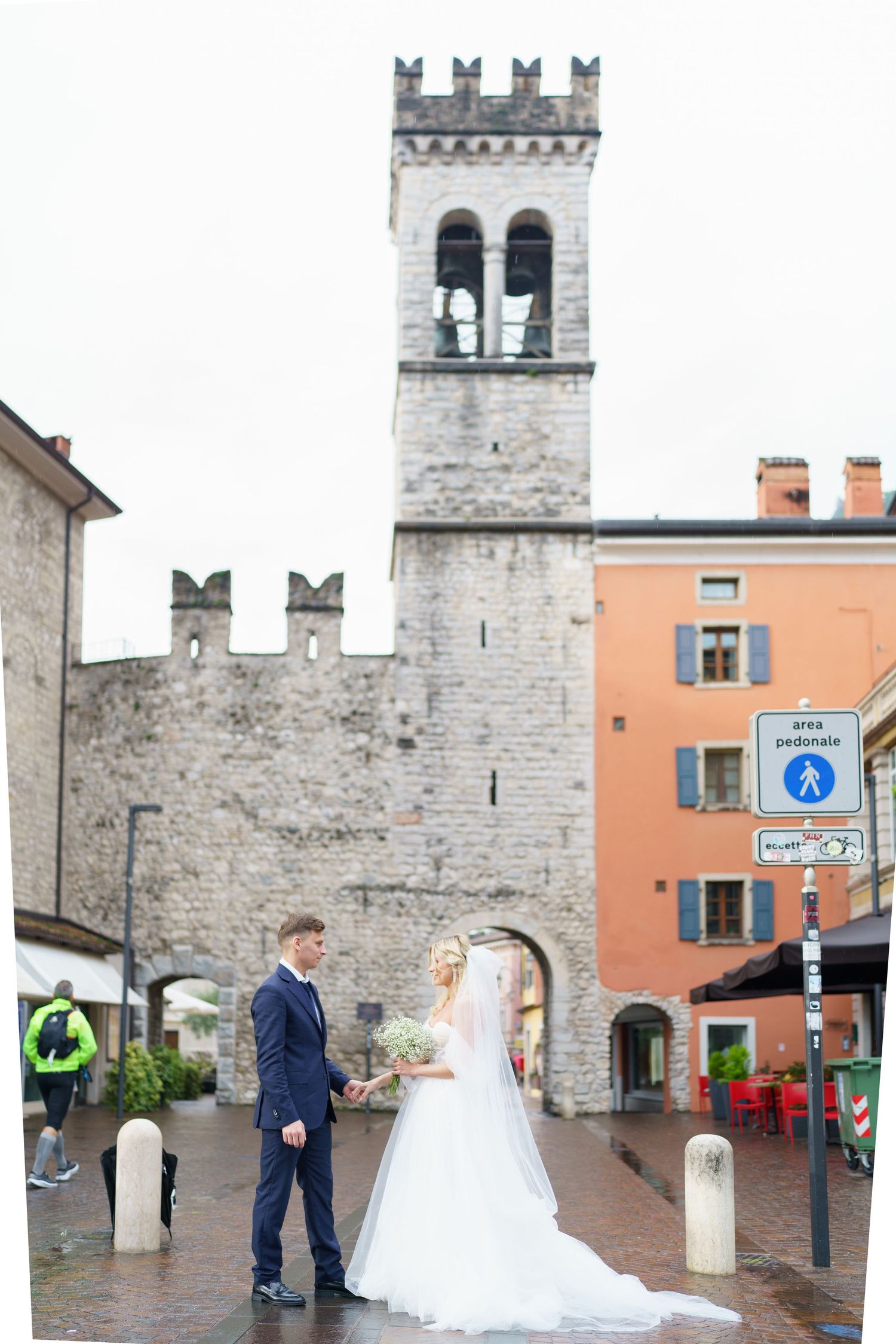 A couple poses near historic stone castle walls and archways in a quaint European town square.