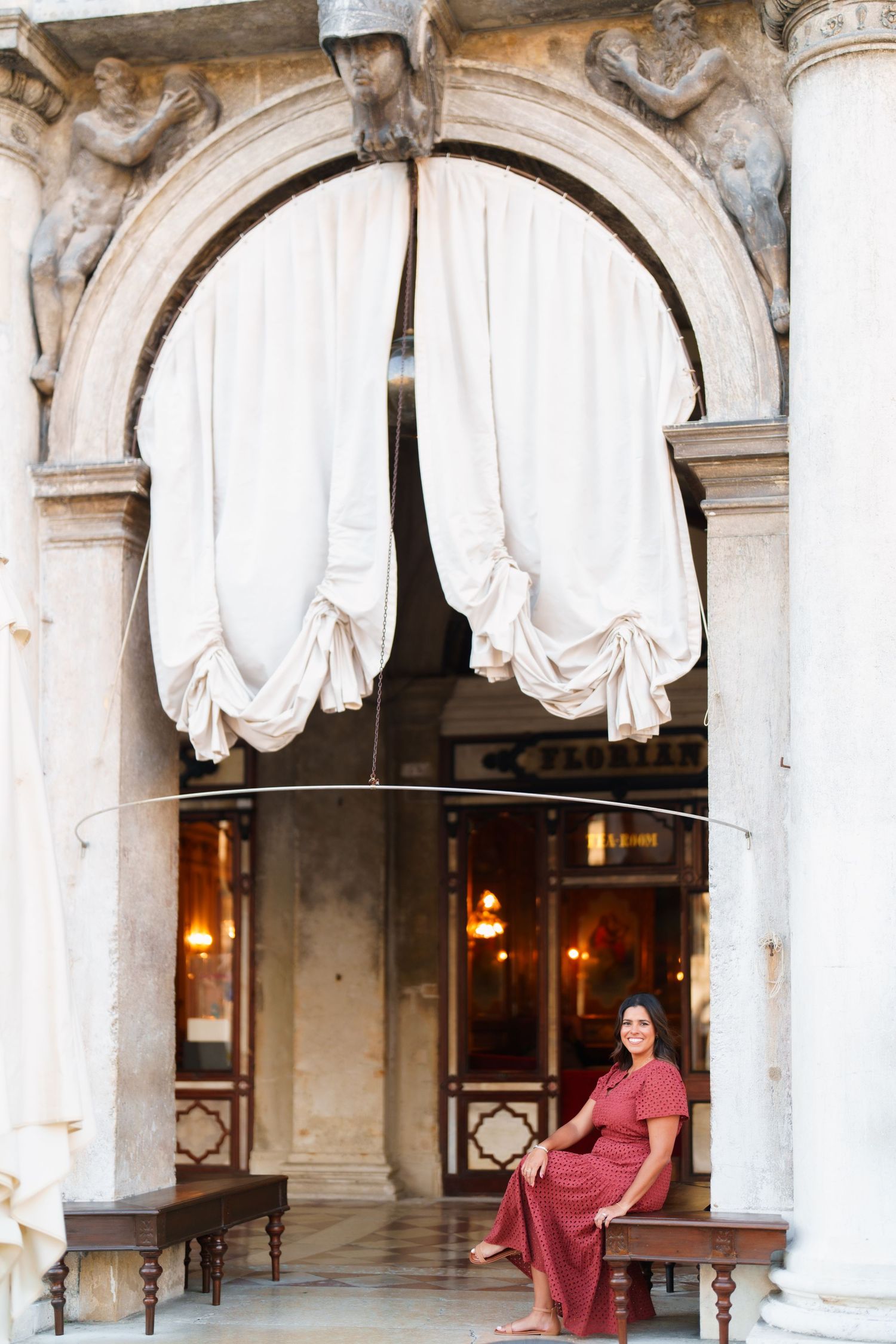 Woman in red dress sitting under ornate arch with white draping curtains at Caffe Florian, Venice.