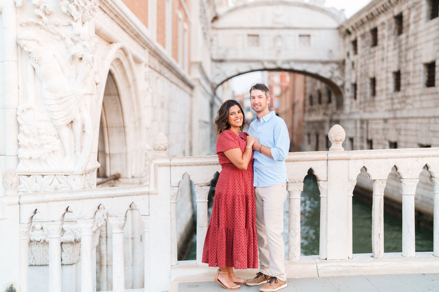 Couple embracing on a bridge in Venice, Italy, with the iconic Bridge of Sighs and ornate architecture in the background.