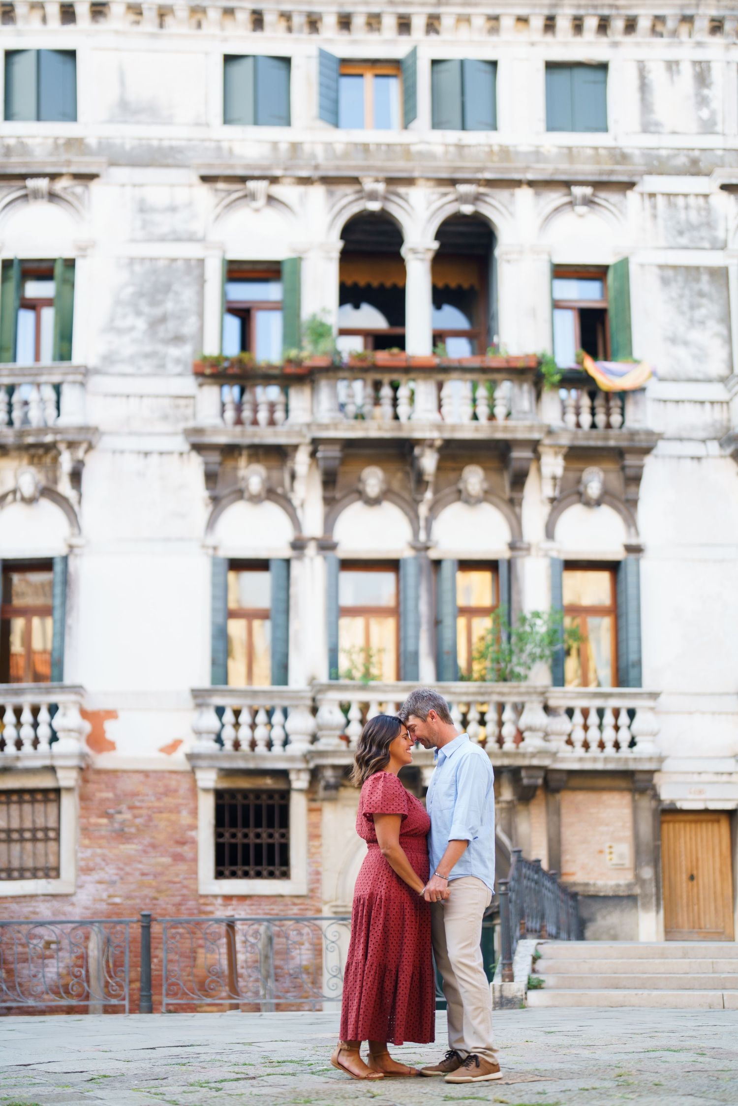 Romantic couple embracing in front of a historic Venetian building with ornate balconies in Venice, Italy.