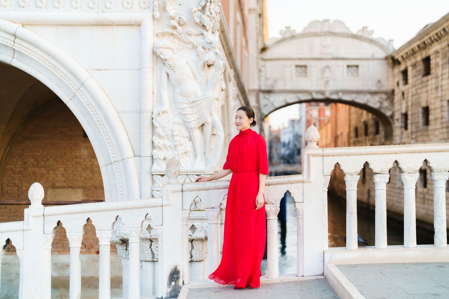 Woman in red gown poses on white bridge near Bridge of Sighs in Venice, Italy.