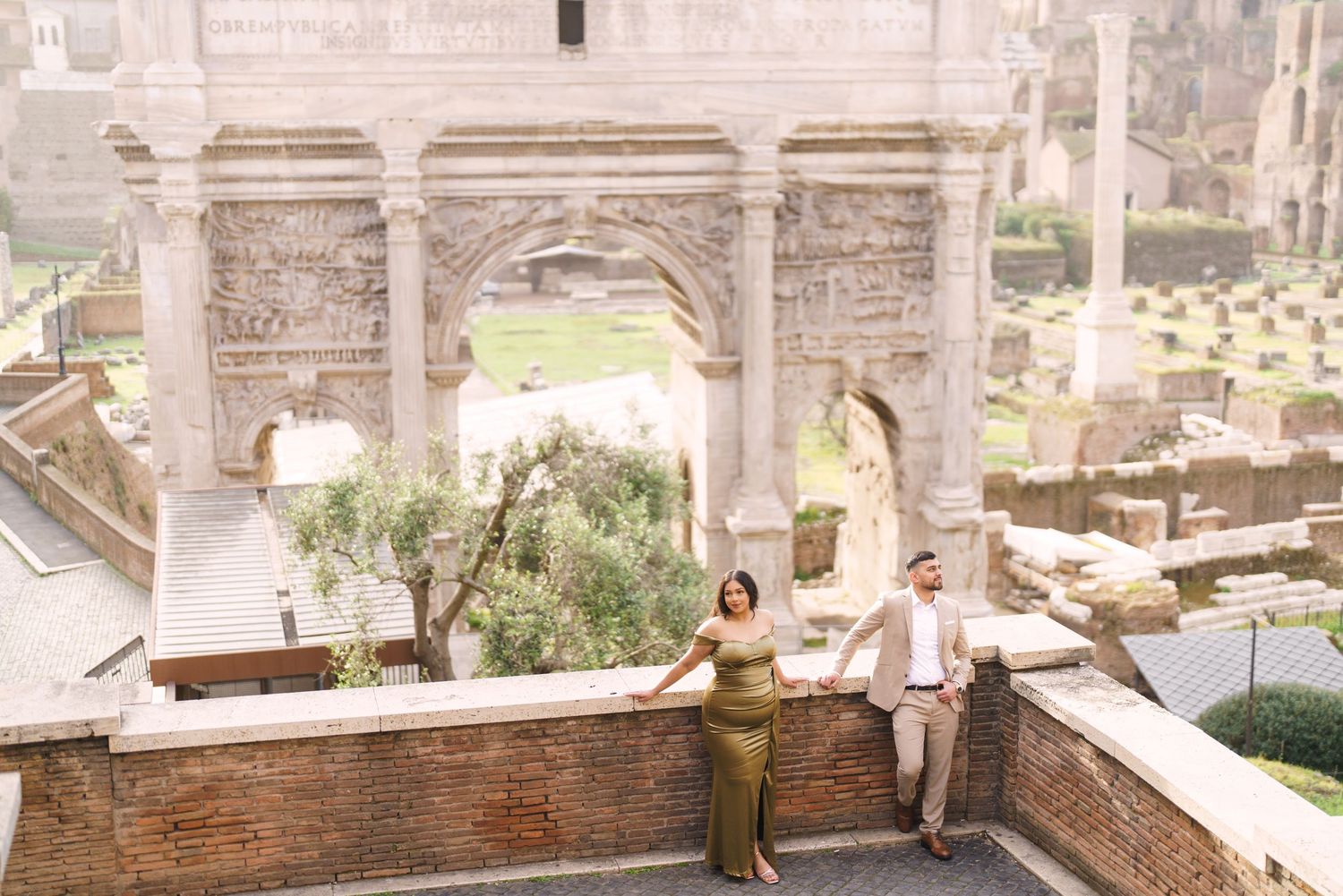 Couple posing at ancient Roman ruins with arched stone architecture and historic Forum in the background.