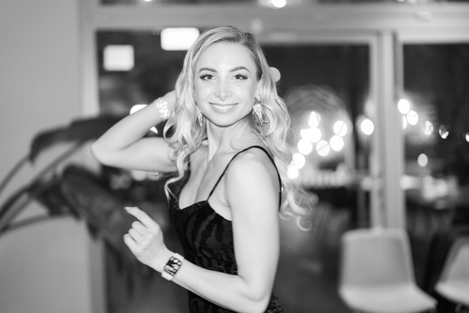Black and white photo of a smiling blonde woman in elegant attire posing gracefully at an upscale indoor event.