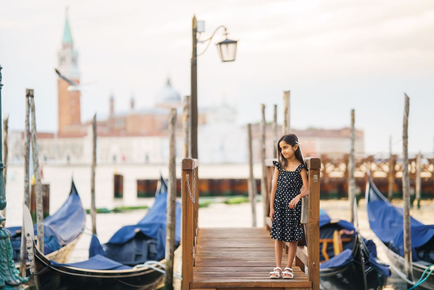 Young girl in polka dot dress standing on Venice gondola dock with San Giorgio Maggiore in background.