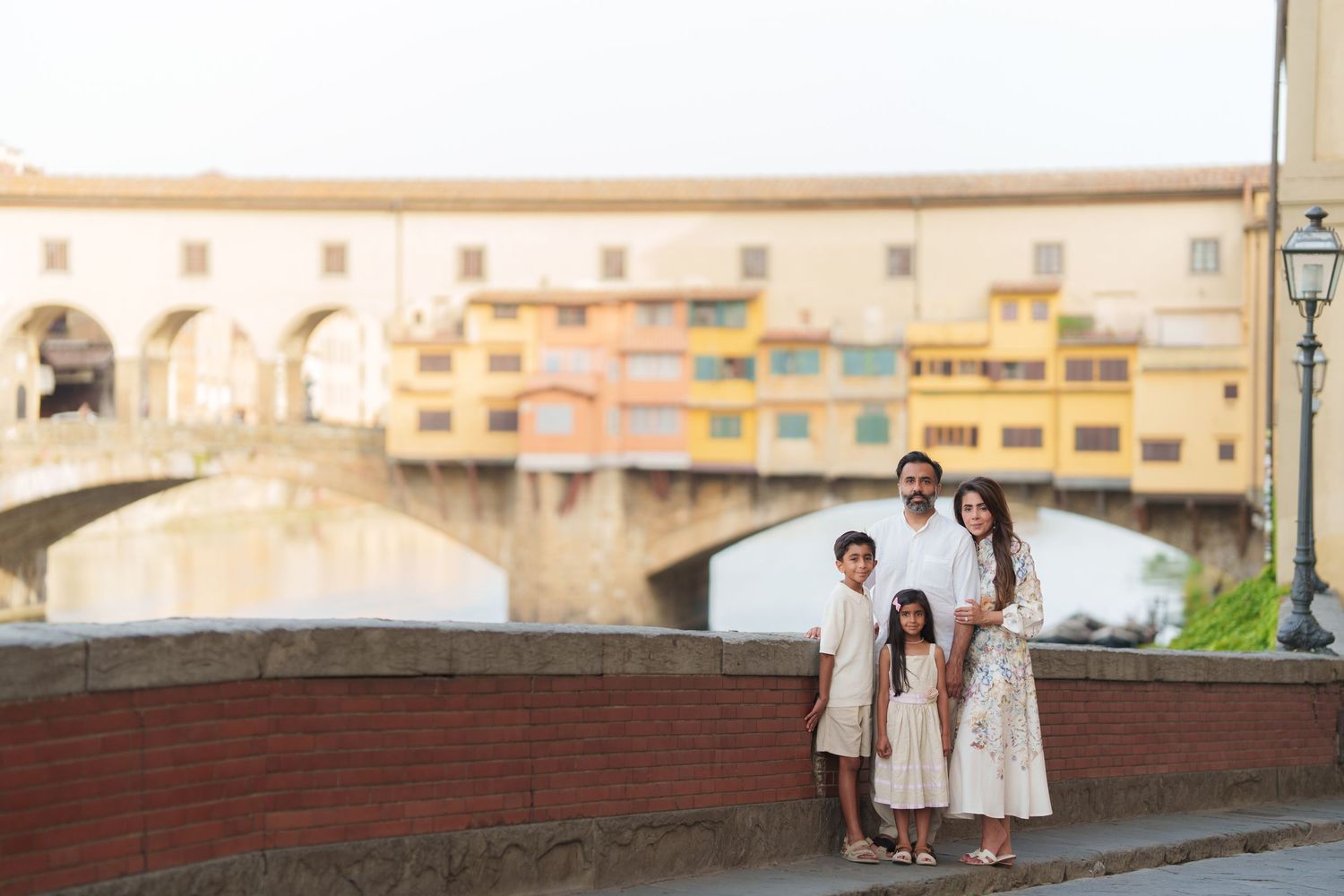 Family of four posing in front of Ponte Vecchio bridge in Florence, Italy, at golden hour.
