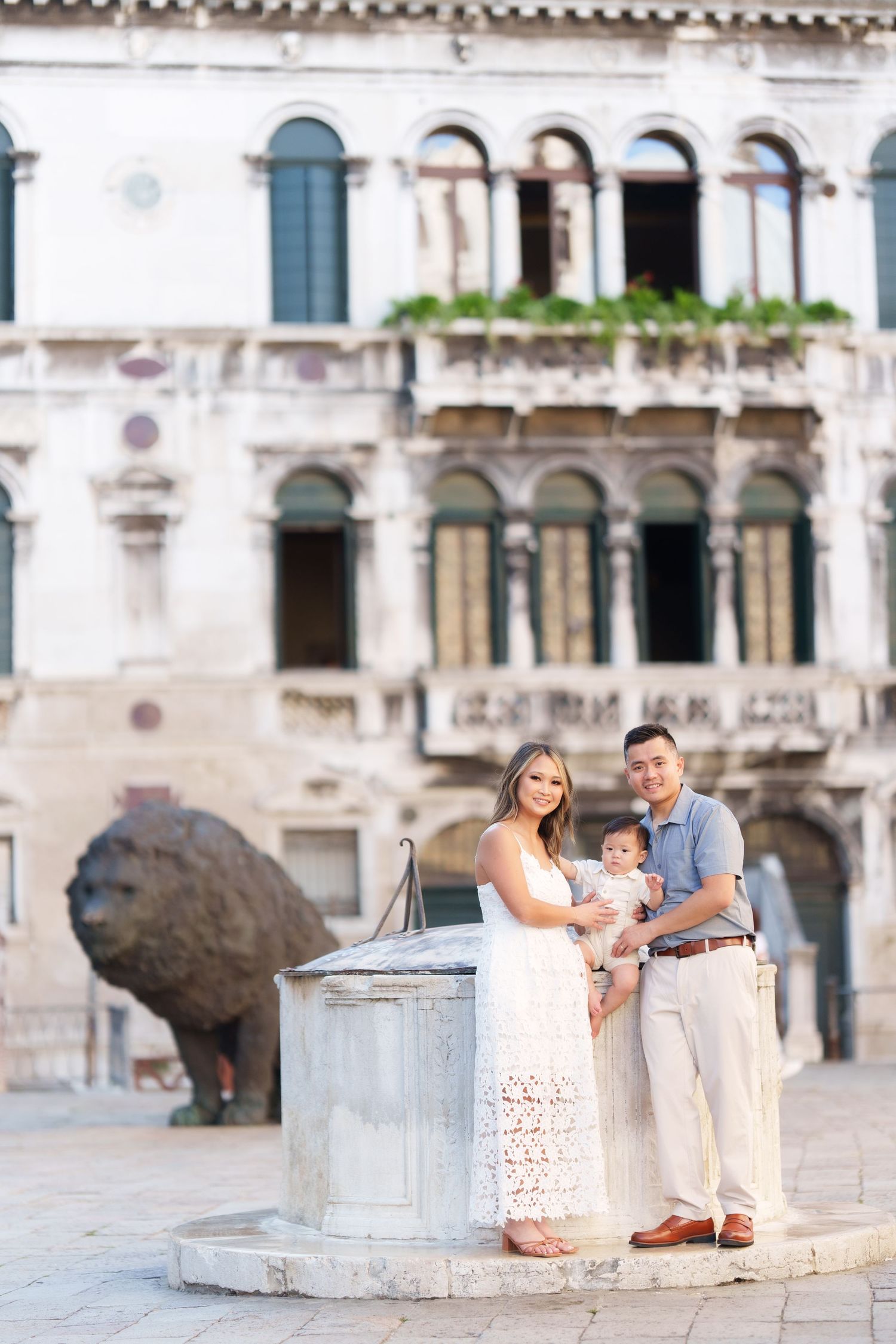 Family of three posing by a stone well in Venice, Italy, with historic architecture in the background.