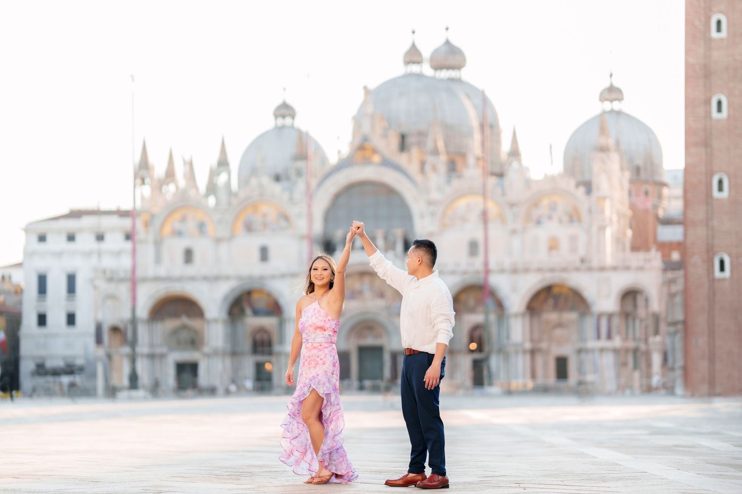 Couple dancing in St. Mark's Square, Venice, woman in pink floral dress, Byzantine basilica backdrop at golden hour.